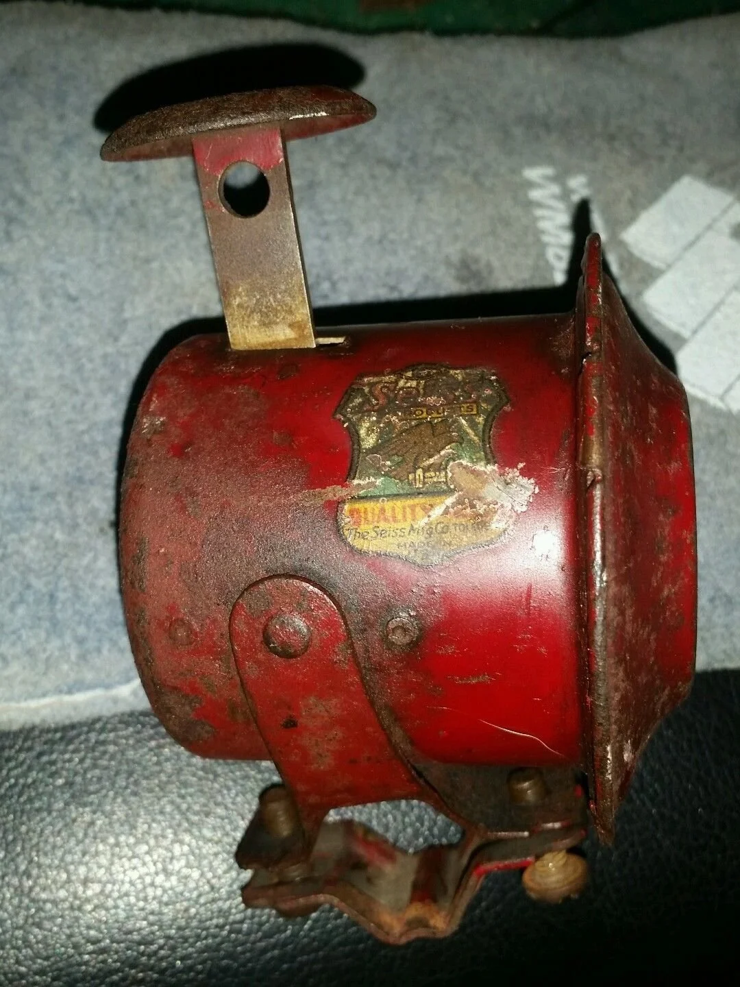 Vintage red metal siren or alarm with old worn label and rusted parts.