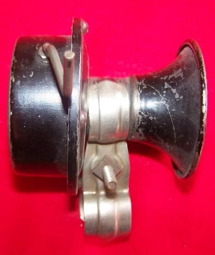 Close-up of a mechanical device with a black cylindrical component, metallic middle section, and a black conical end against a red background.