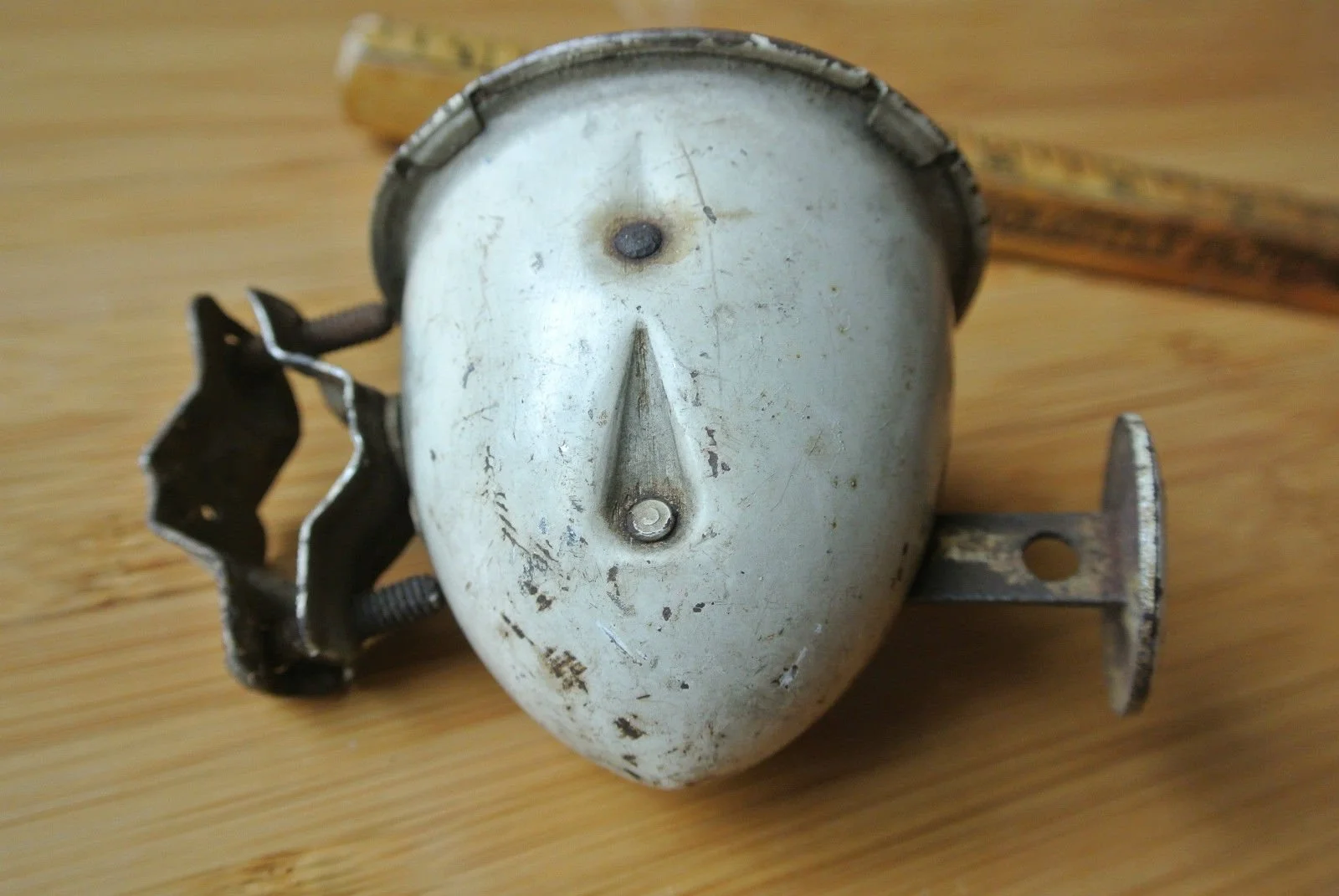 A vintage headlight with a face-like design, featuring a single screw for a nose, a round bolt for an eye, and a rounded shape resembling a face, placed on a wooden surface.
