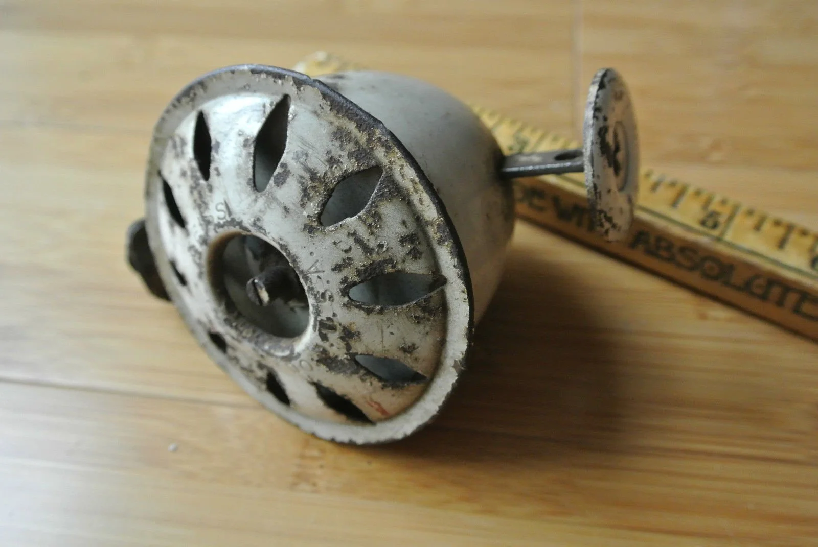 An old, rusty metal heater element with a cylindrical shape, lying on a wooden surface, with a ruler next to it showing measurements.