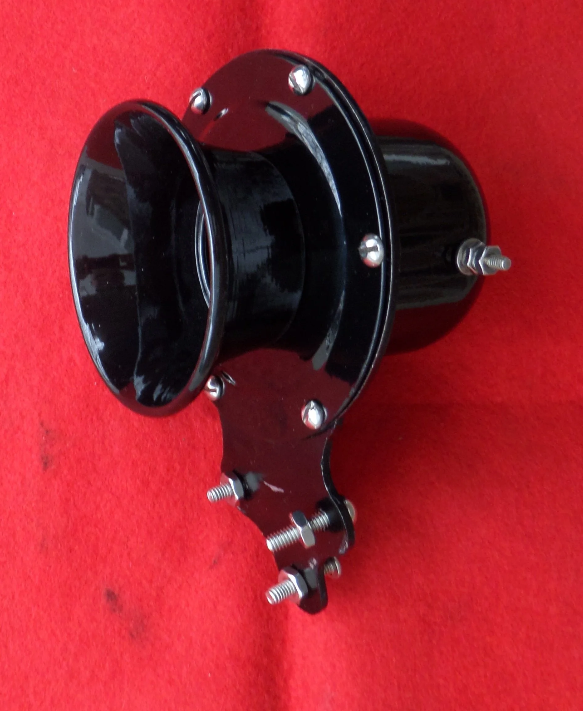 A black motorcycle speedometer with mounting brackets and screws on a red surface.