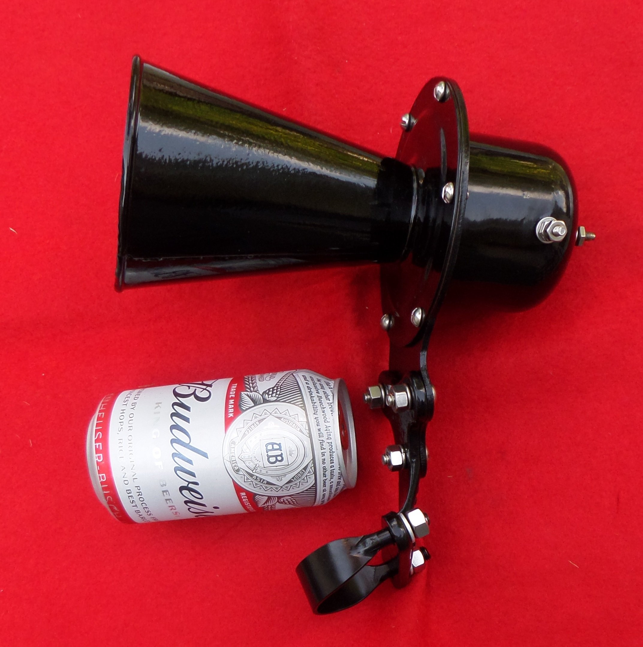 A black spotlight with a circular mounting base, positioned next to a Budweiser beer can on a red background.