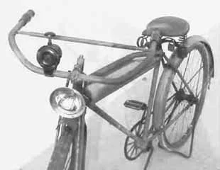 Black and white photo of a vintage bicycle with a large front headlight and a bell, positioned at an angle.