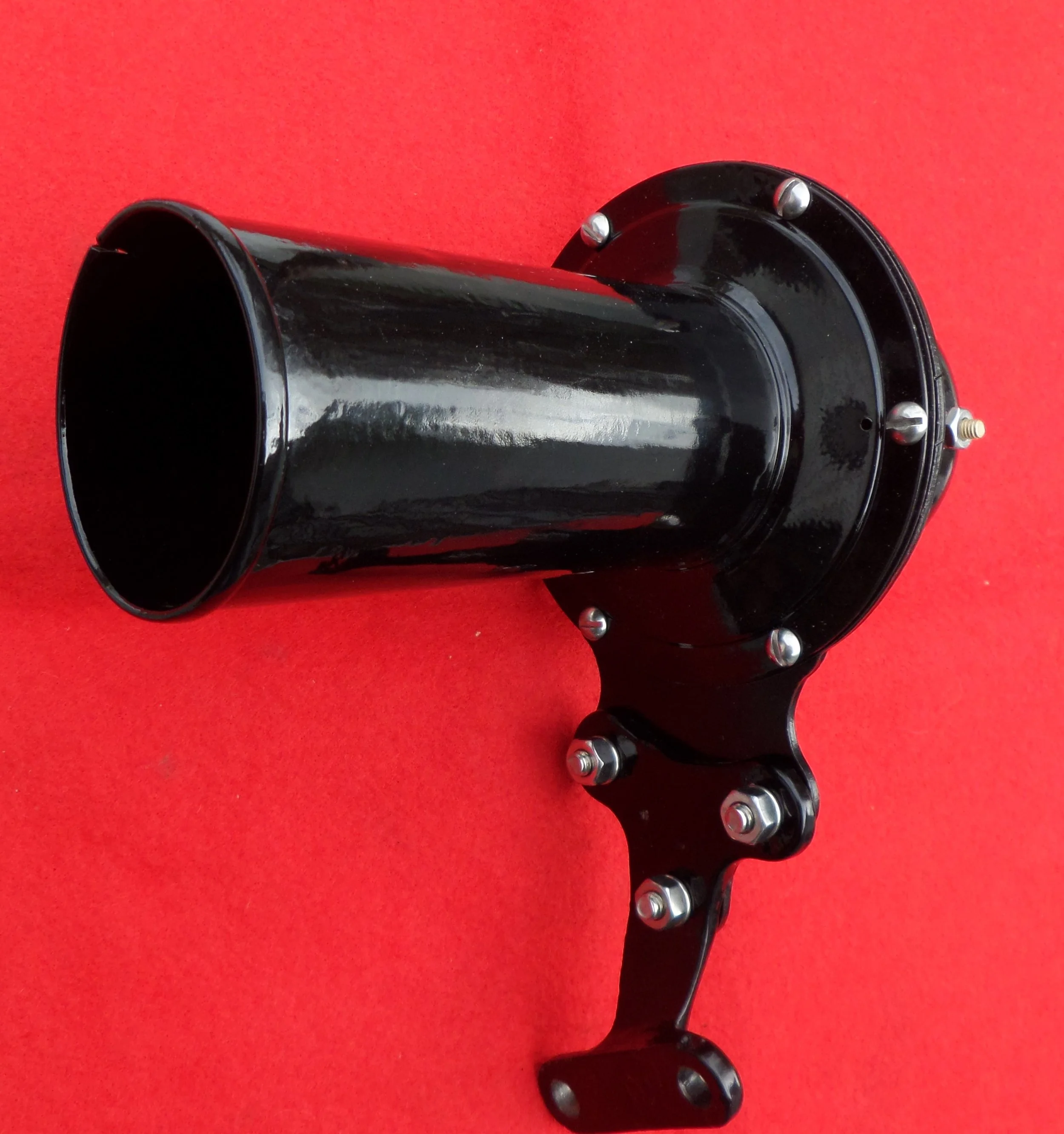 Black metal camera mount with a cylindrical tube, mounted on a red background.