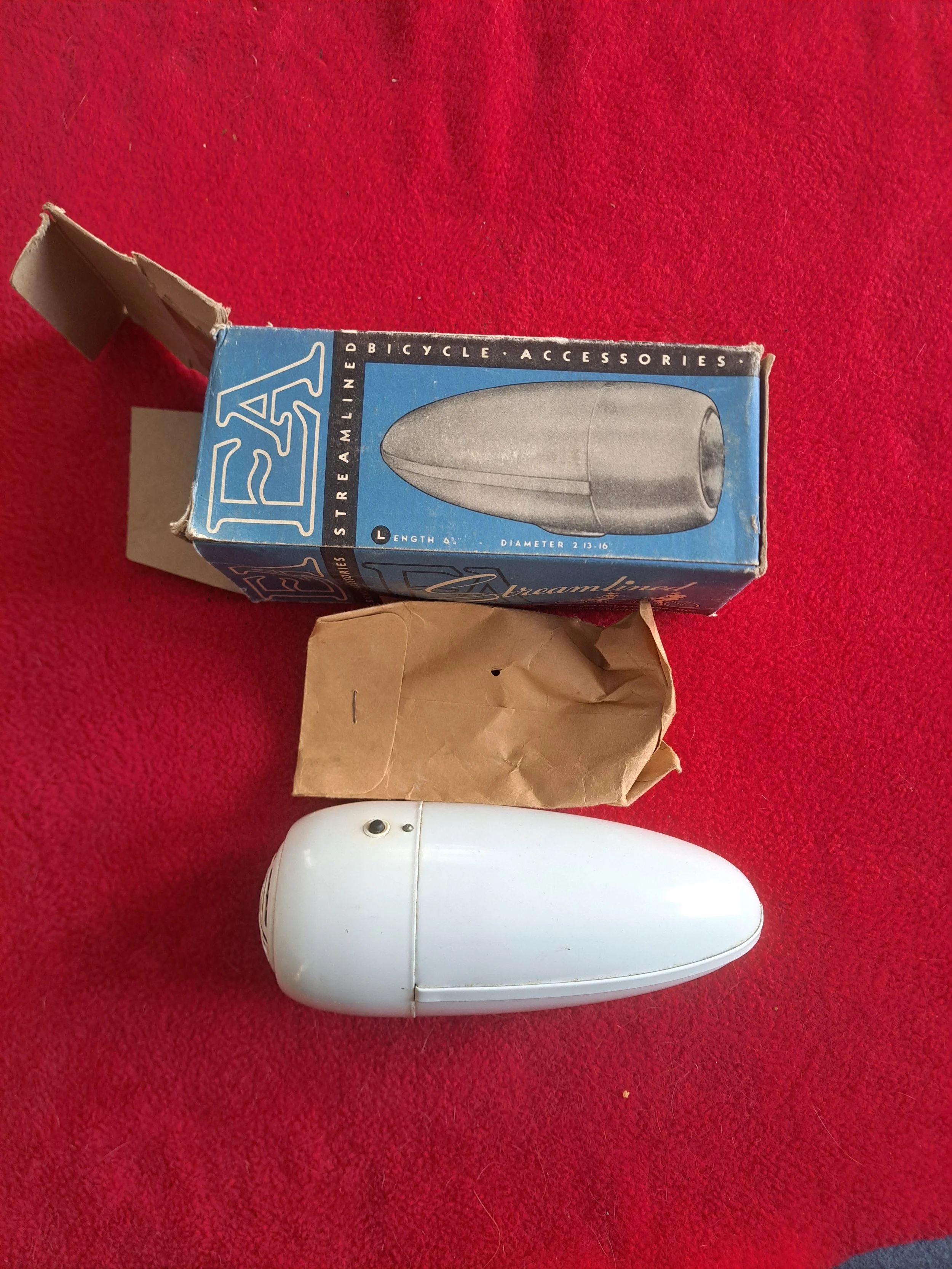 A white bicycle reflector light with a side switch, a small cardboard box, and a blue box for a bicycle accessory, all placed on a red fabric surface.