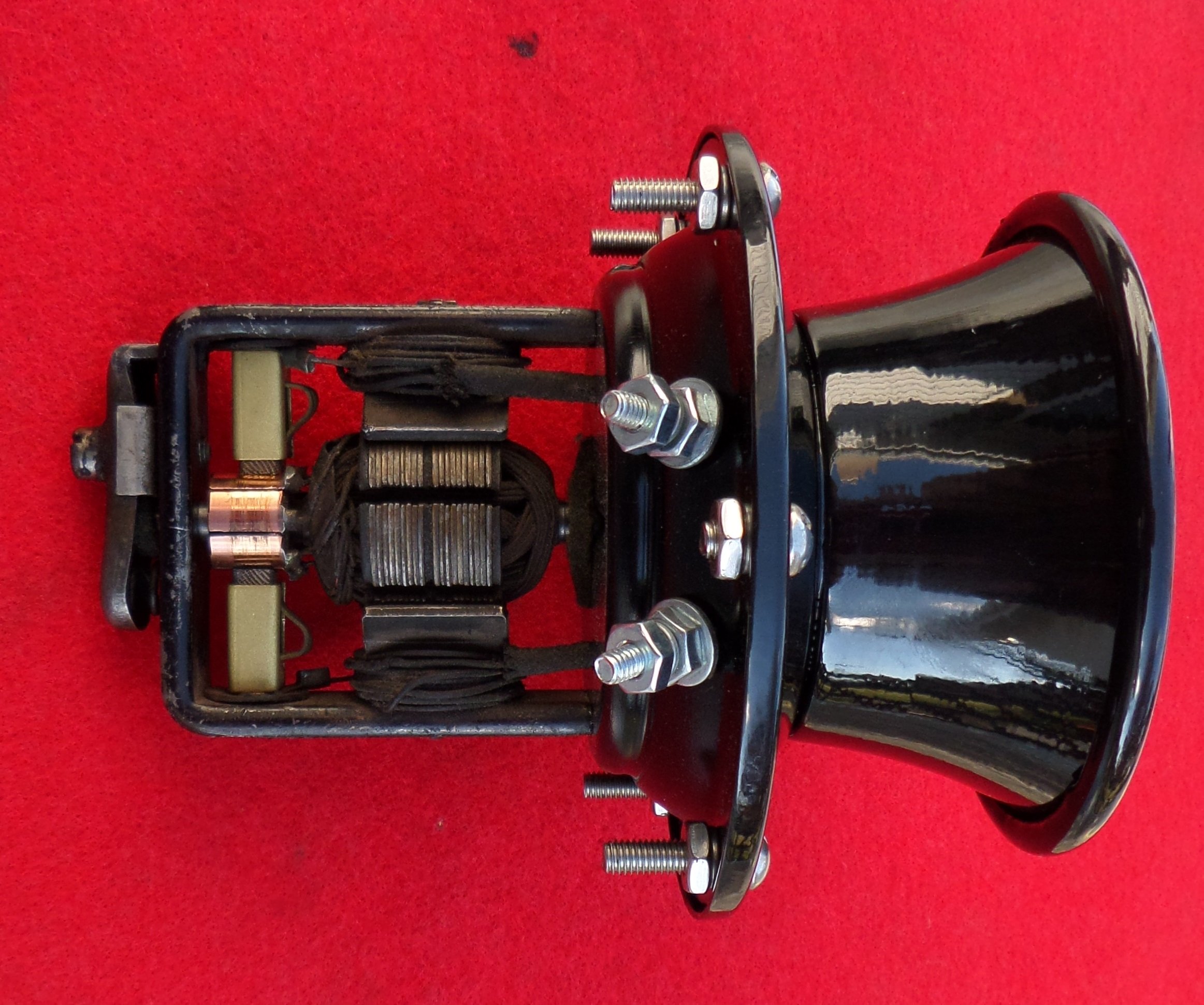 An electrical device with coils, wires, and metal bolts, mounted on a black and metallic structure, with a black lampshade or reflector attached.