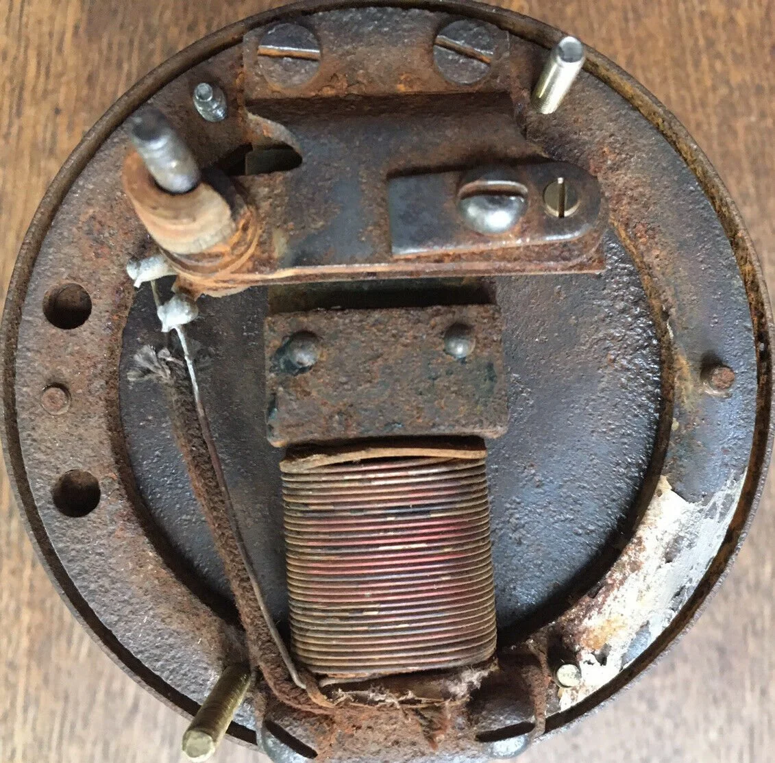 A rusty, worn-out electric motor with visible coils, mounting bolts, and electrical components.