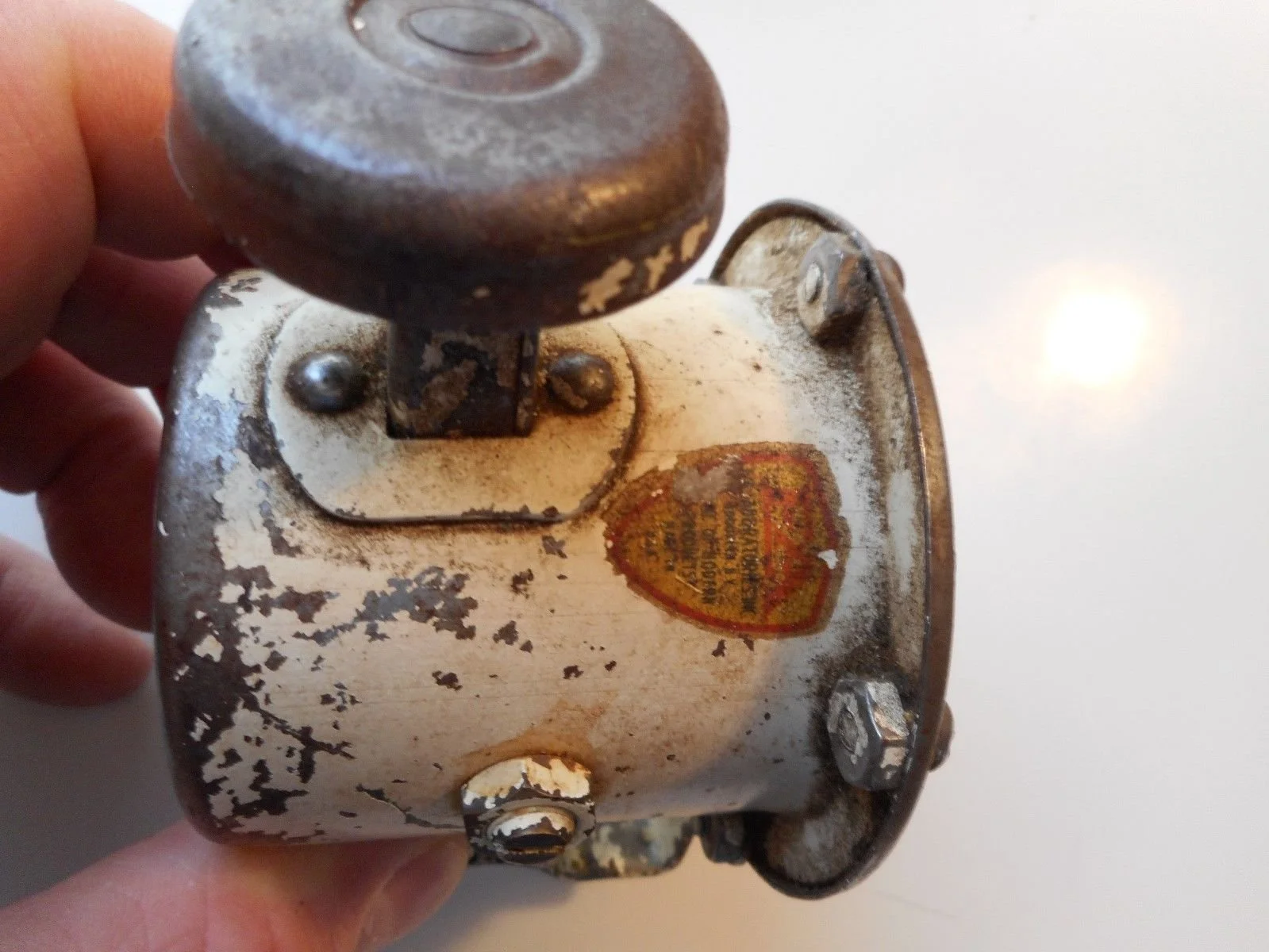A vintage, weathered metal object with a worn label and peeling paint, held by a person's hand.
