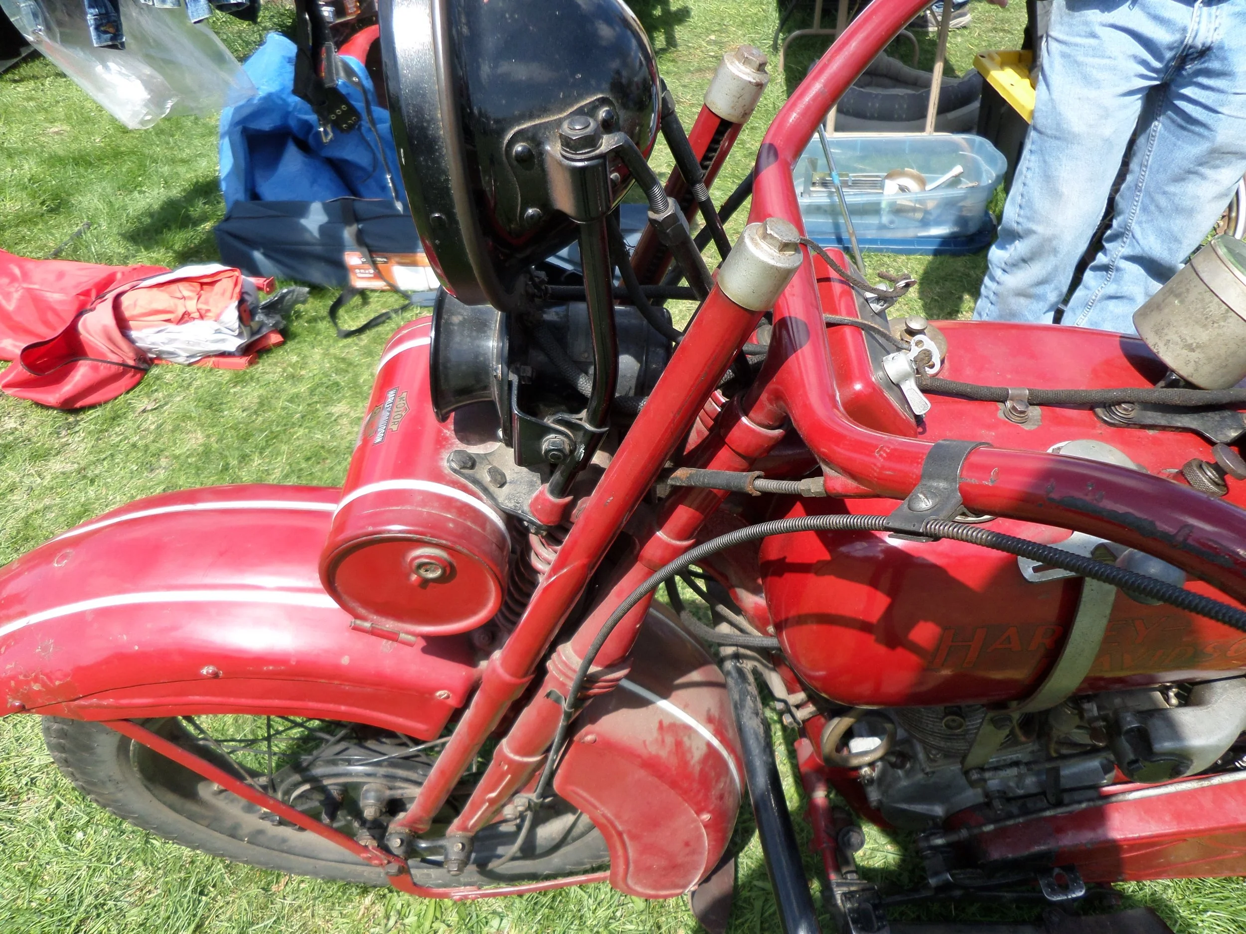 Old red Harley Davidson motorcycle with parts and tools around it, outdoors on grass.