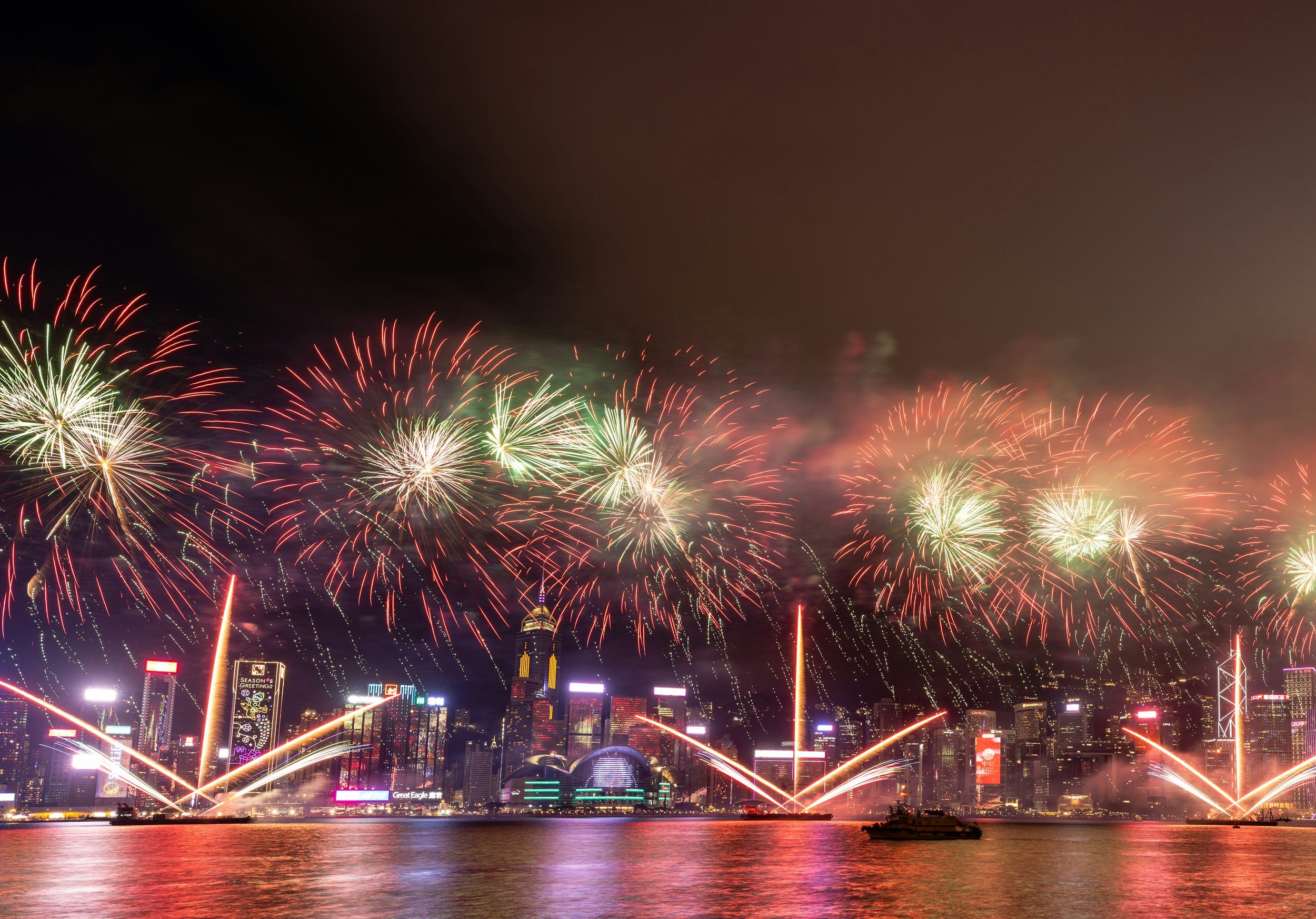 Fireworks display over a city skyline at night, with reflections on water.