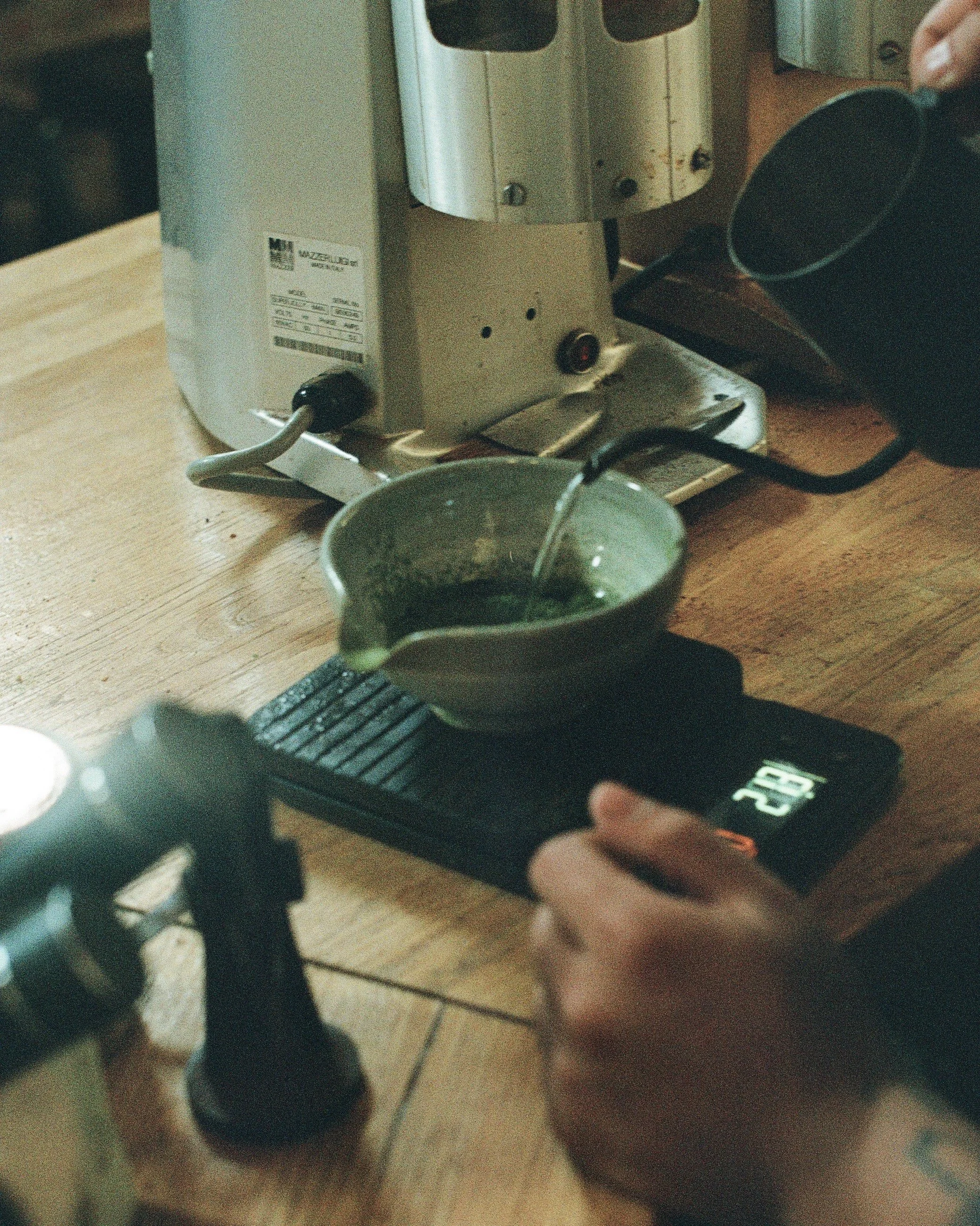 Pouring espresso from a portafilter into a cup on a digital scale in a coffee shop kitchen.