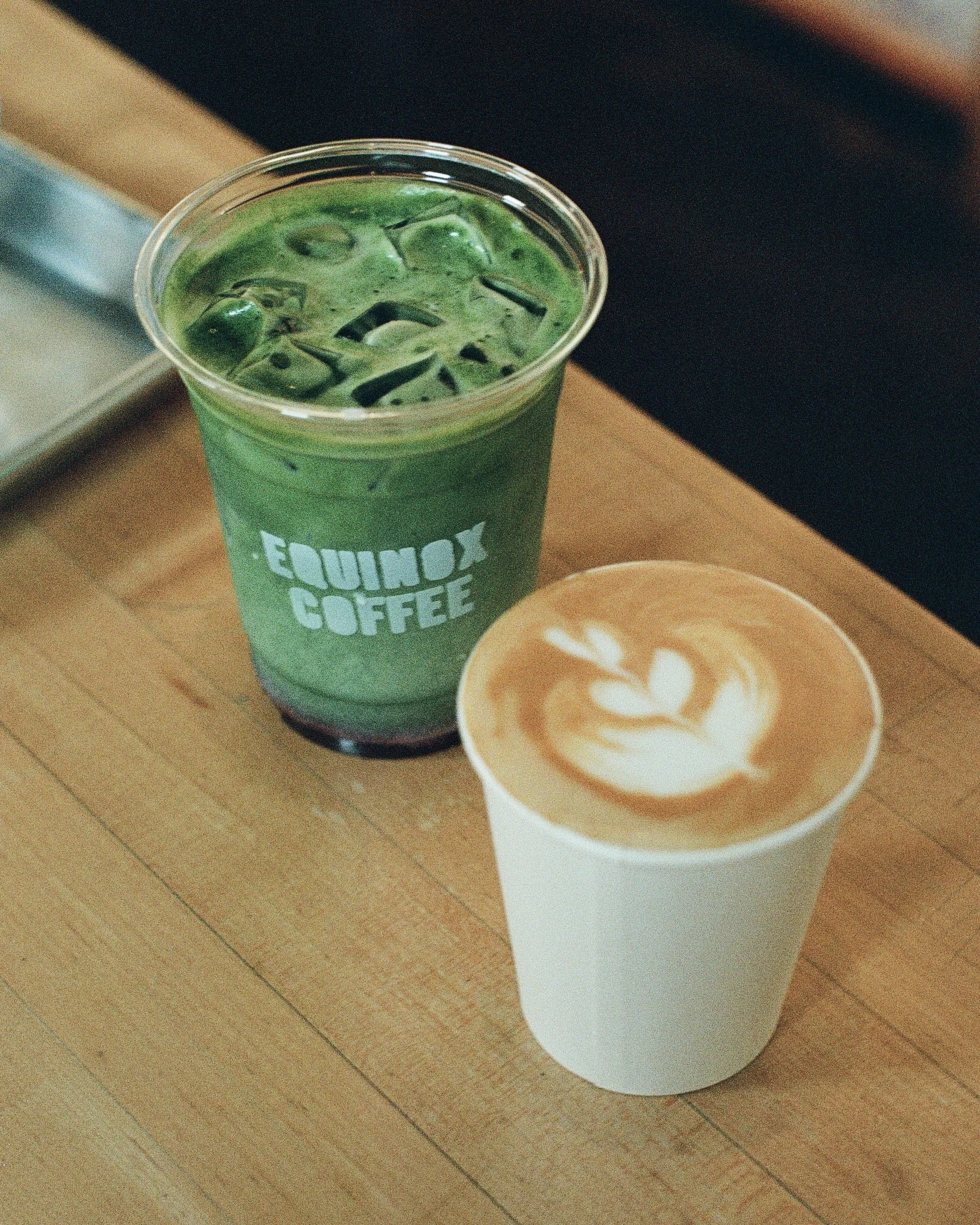 Ice green tea and a latte with latte art on a wooden table.