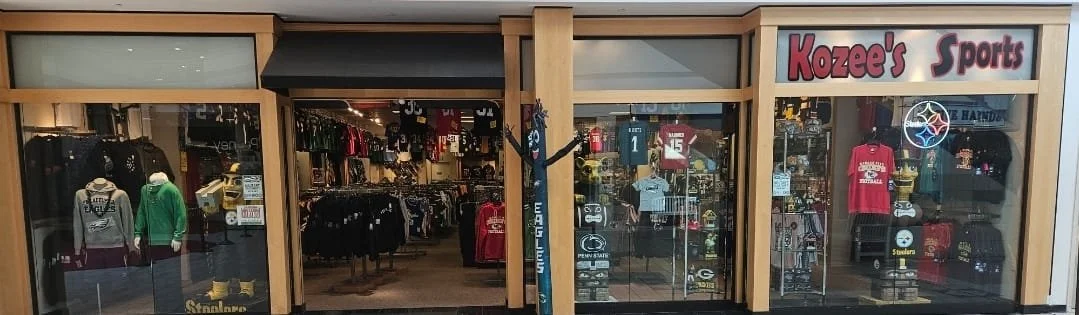 Exterior view of Kozee's Sports store with display windows showcasing sports apparel and gear, the store's sign above the entrance reading Kozee's Sports.