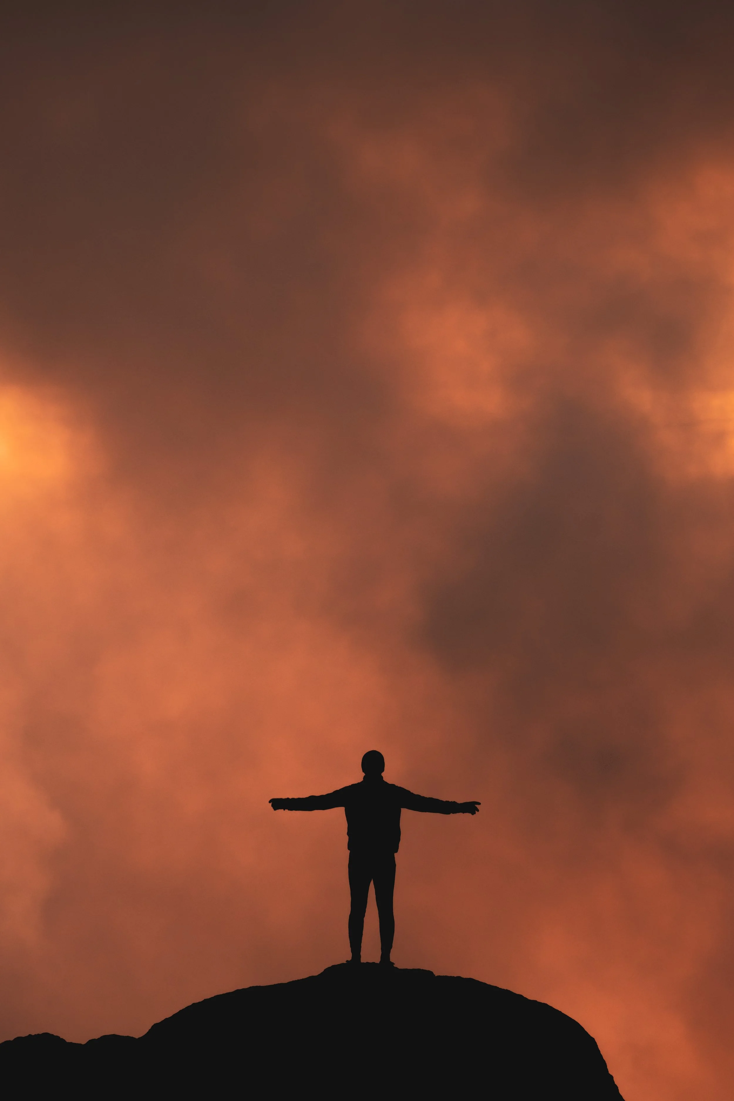 Silhouette of a person standing on a rock with arms outstretched, sunset sky with orange and purple clouds in the background.
