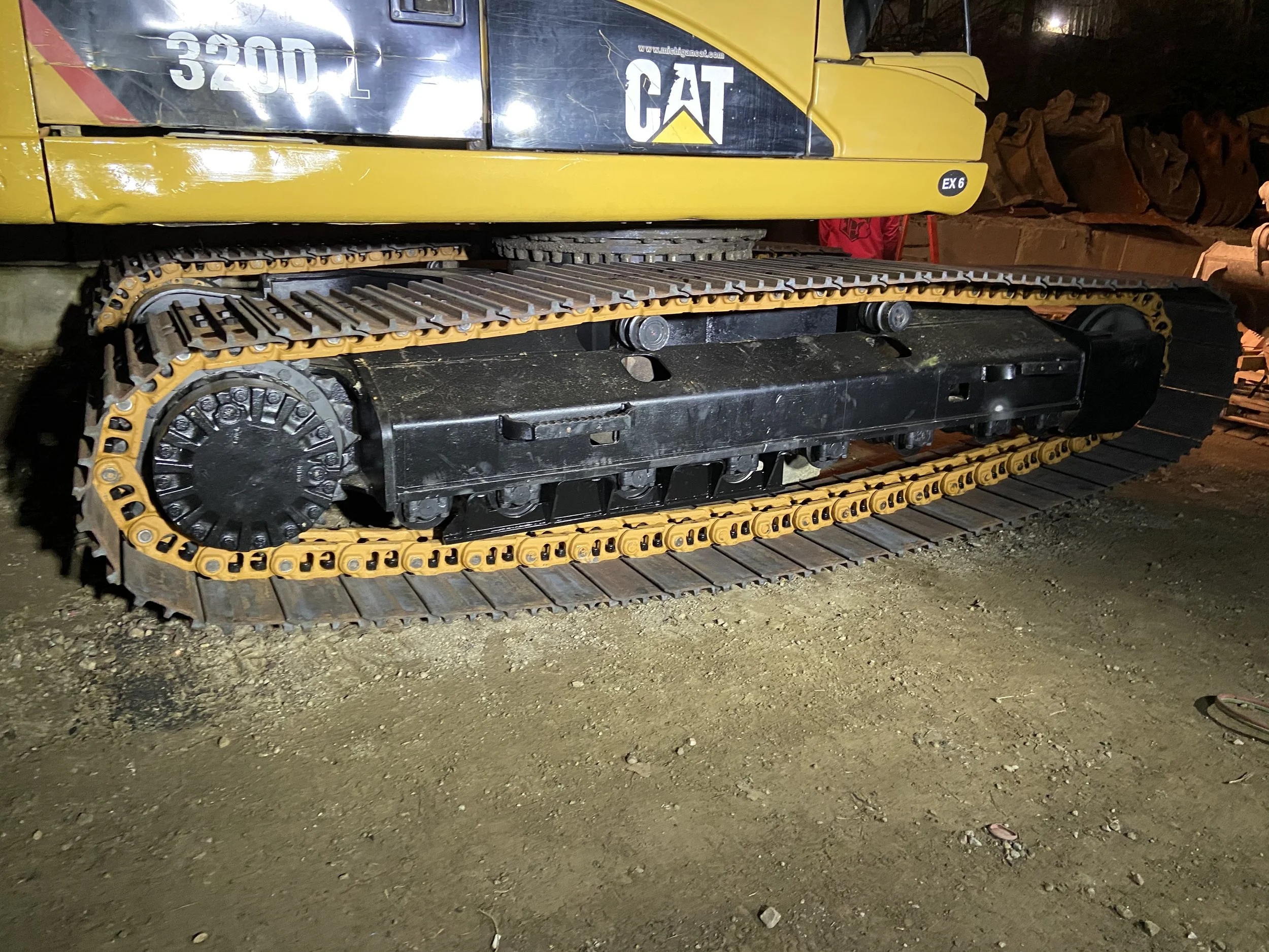 Close-up of a yellow and black Caterpillar excavator, showing the track and undercarriage which has just been replaced, with the model number 320DL