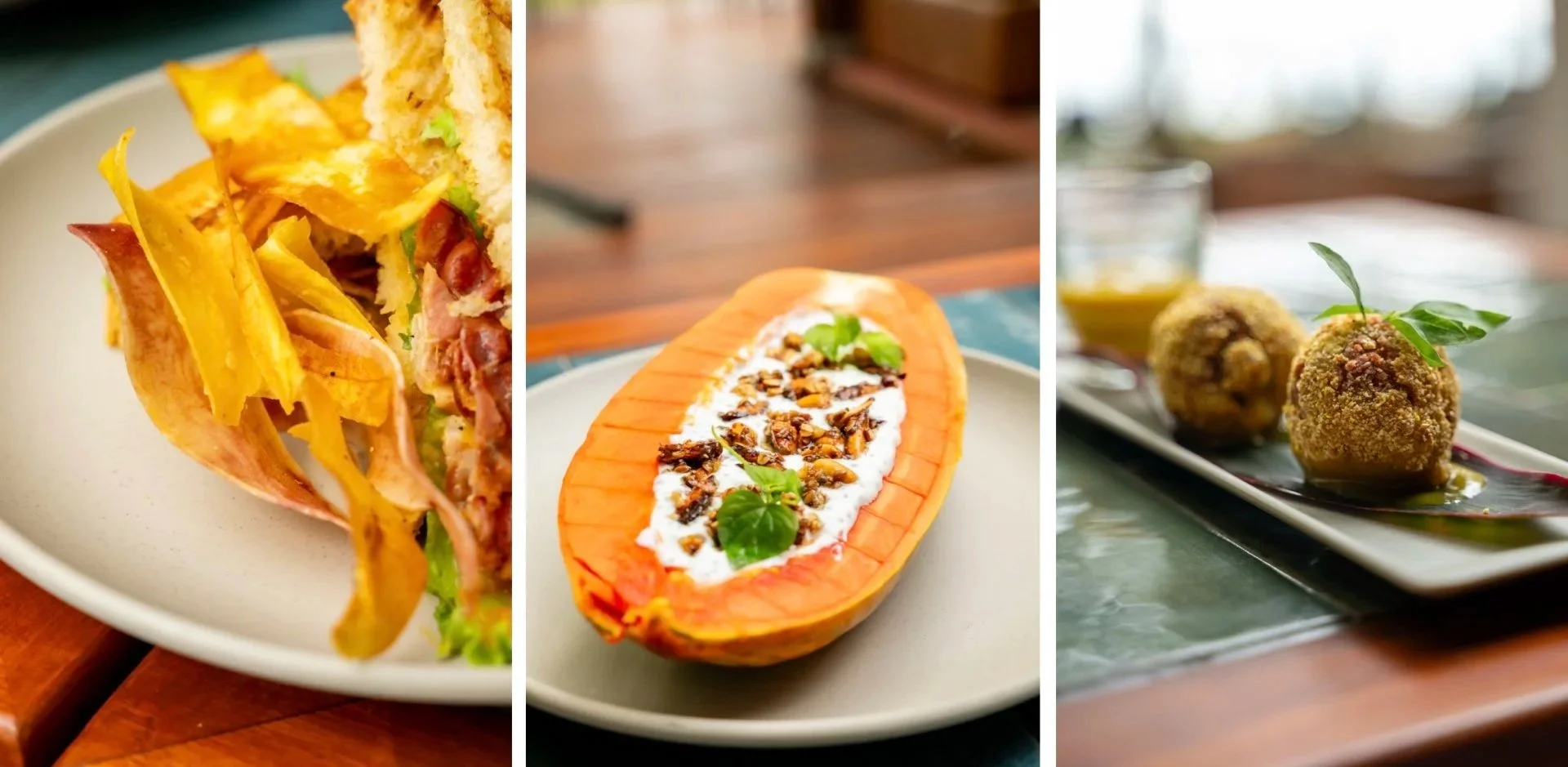Three different dishes: a sandwich with potato chips, a halved papaya with yogurt and nuts, and two fried croquettes garnished with basil leaves on a black and red plate.