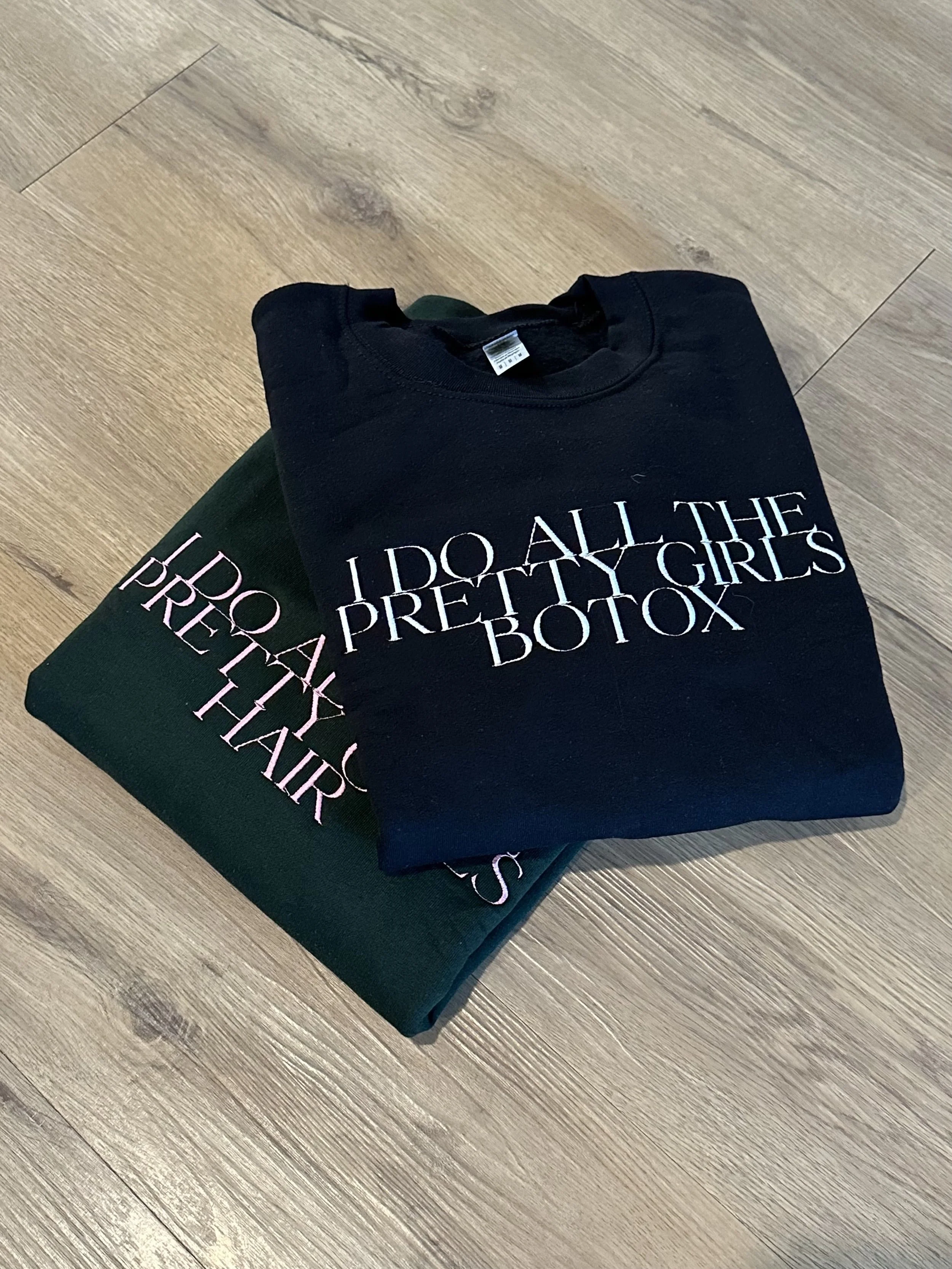 Two folded graphic T-shirts, one black and one green, on a wooden floor, both with text about beauty procedures.