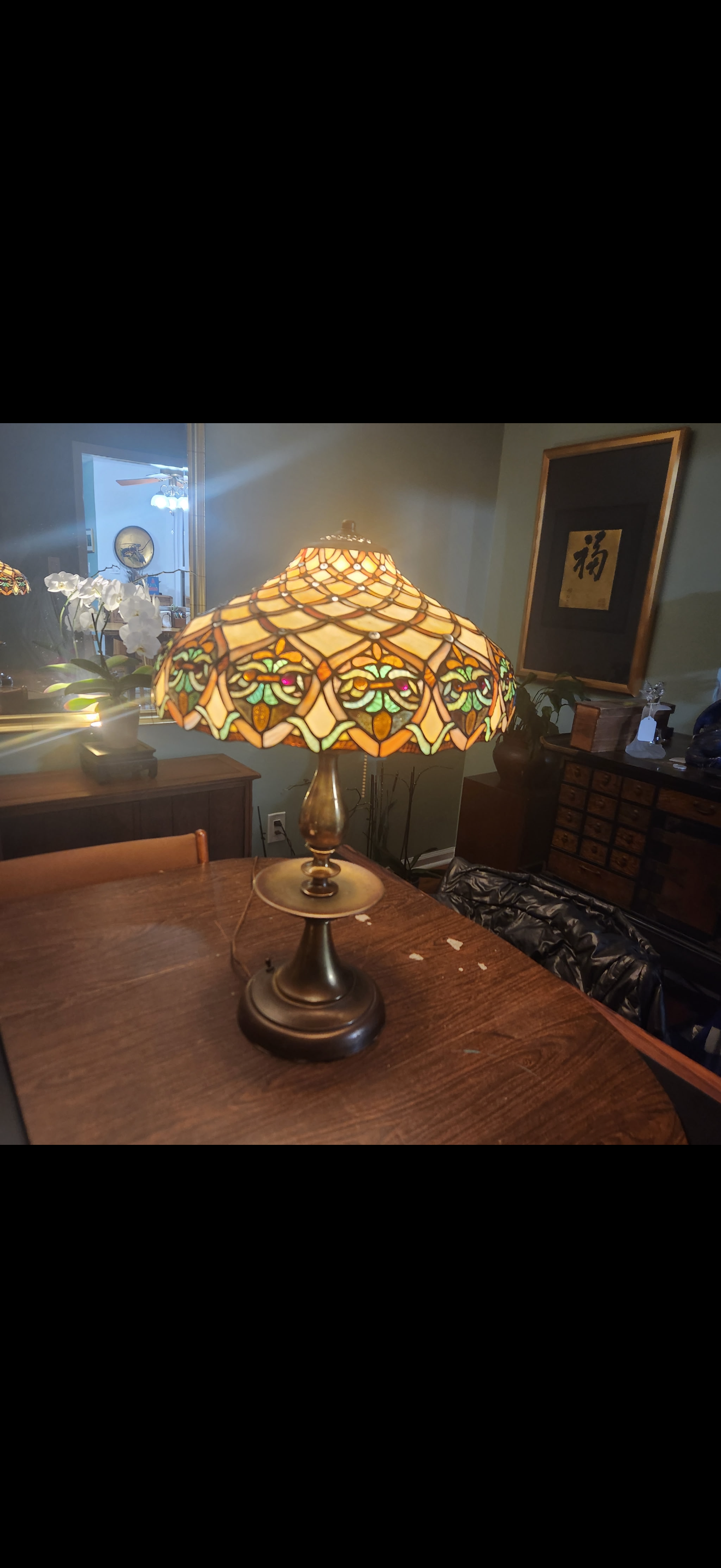A decorative Tiffany-style table lamp with a stained glass shade featuring floral patterns, placed on a wooden dining table.