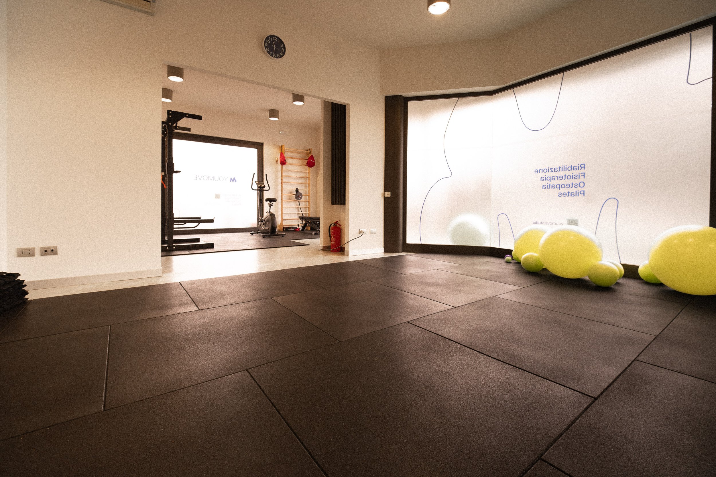 Finestra e parete con attrezzature da palestra, palloni di gomma verdi, e una parete con adesivi e scritte in lingua italiana.