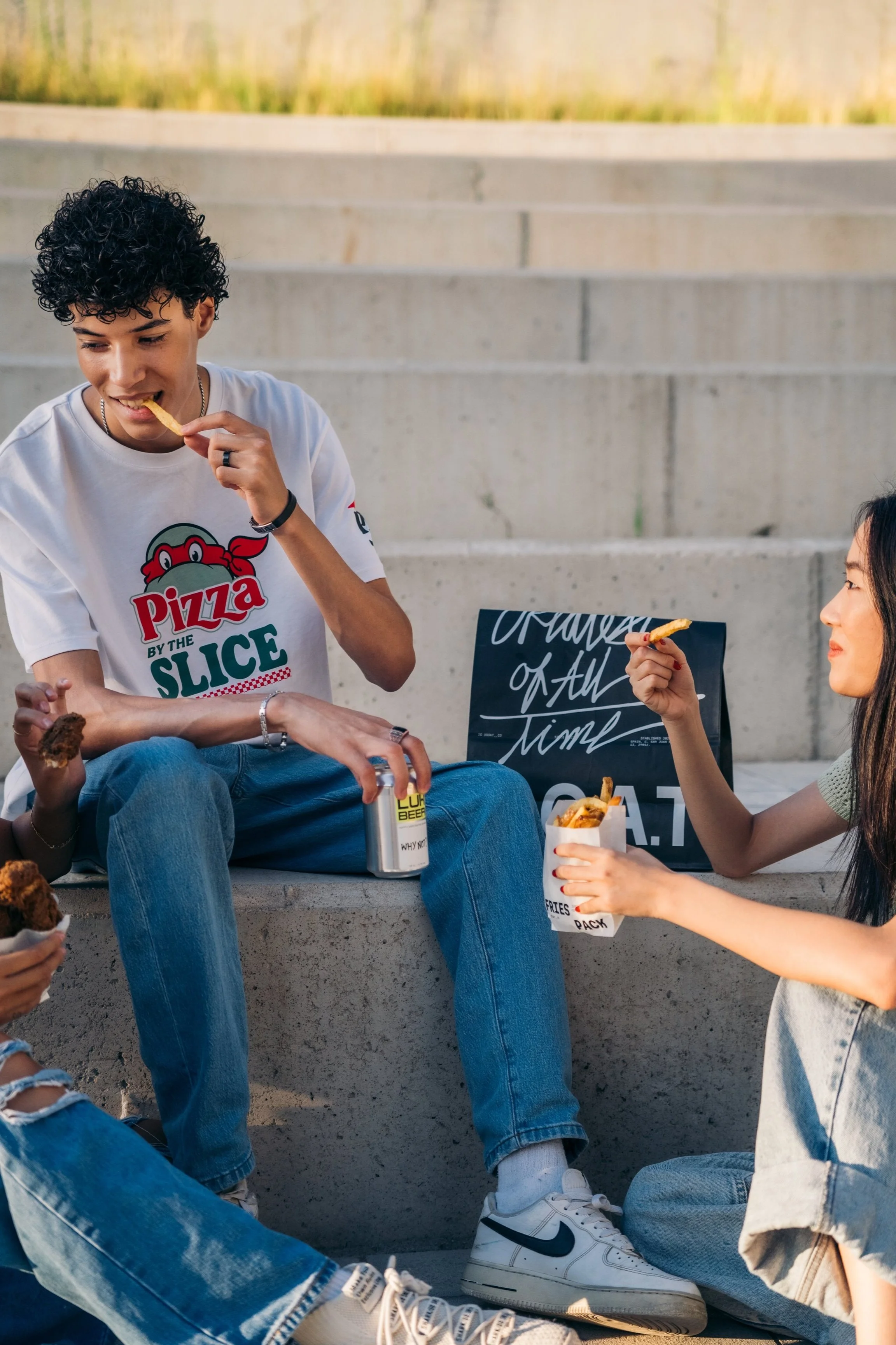 Grupo de amigos comendo comida rápida, como papas fritas y pollo frito, en un espacio abierto con escaleras de cemento de fondo.