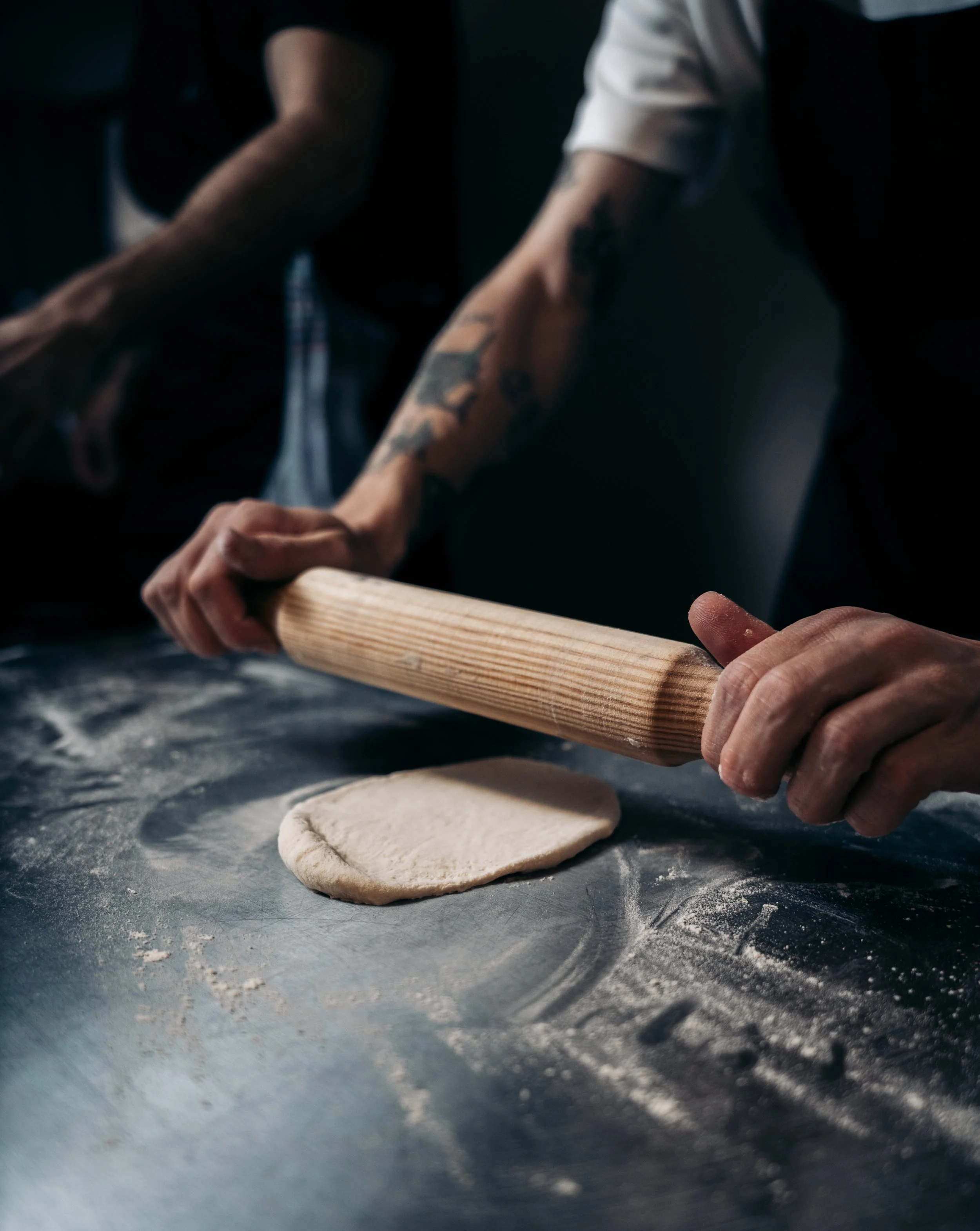 Persona estirando masa de pan con un rodillo de madera en una mesa en una cocina