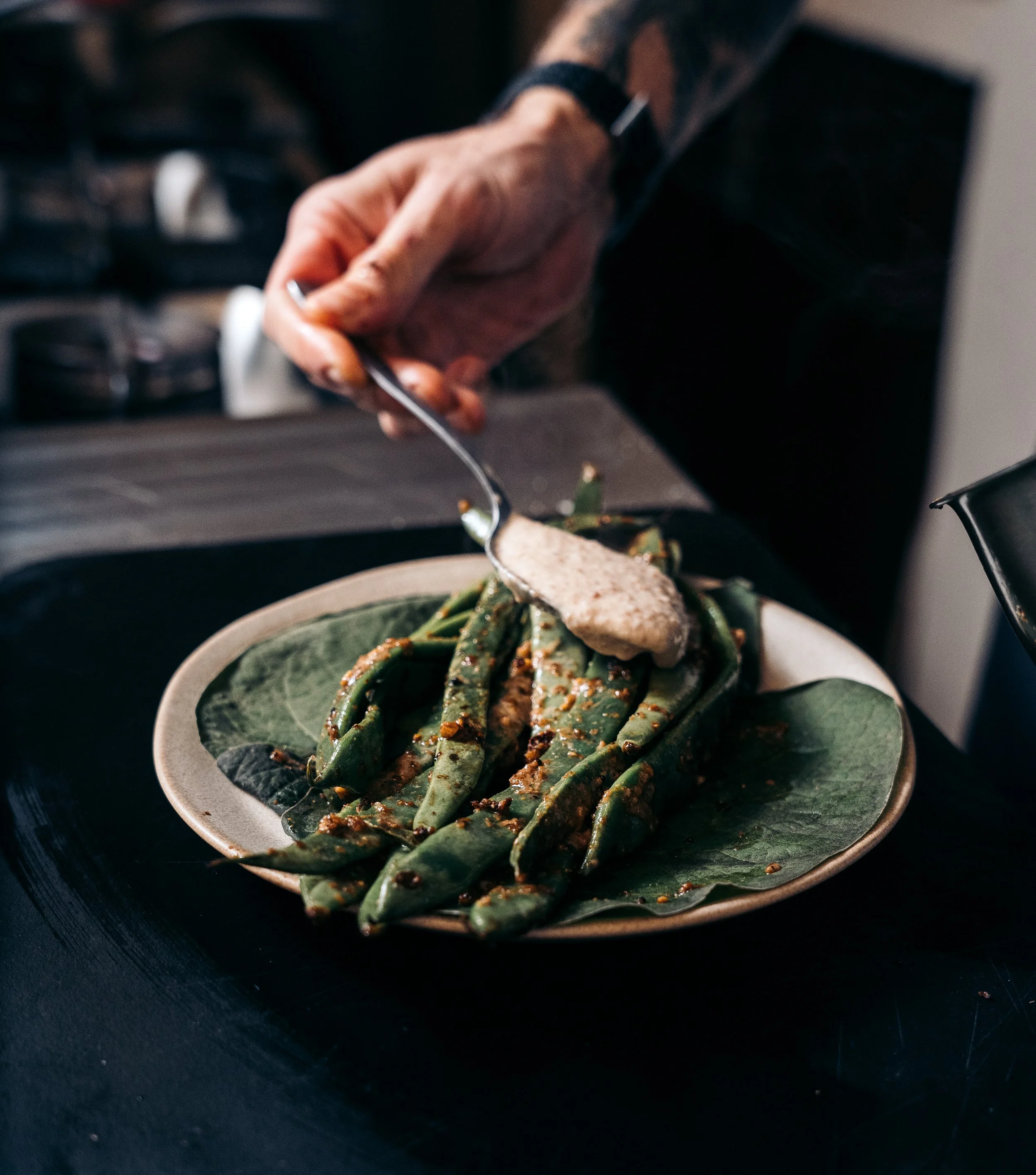 Persona sirviendo salsa sobre frijoles verdes en un plato
