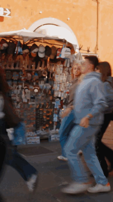 Personas caminando cerca de un puesto con artículos de souvenirs y accesorios en una calle animada.