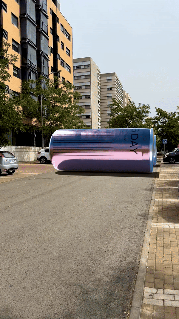 Una estructura que parece una lata gigante de color arcoíris en una calle, con edificios altos y árboles alrededor.
