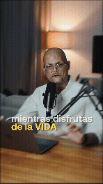 Hombre sentado frente a un micrófono en una oficina, con lámpara y cortinas al fondo.