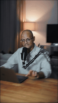 Persona hablando en micrófono en un estudio, con fondo de lámpara y televisión.