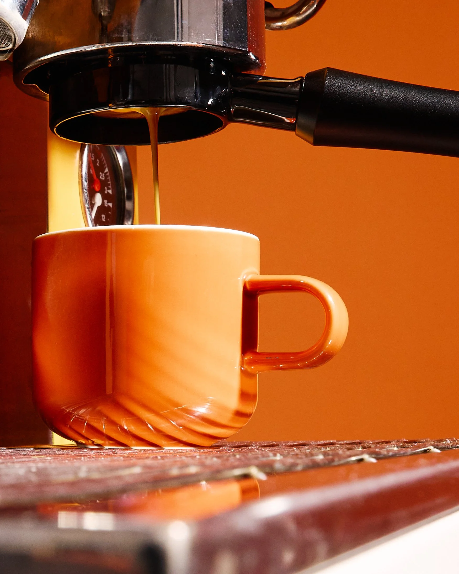 Coffee being brewed into a peach-colored ceramic mug using an espresso machine.