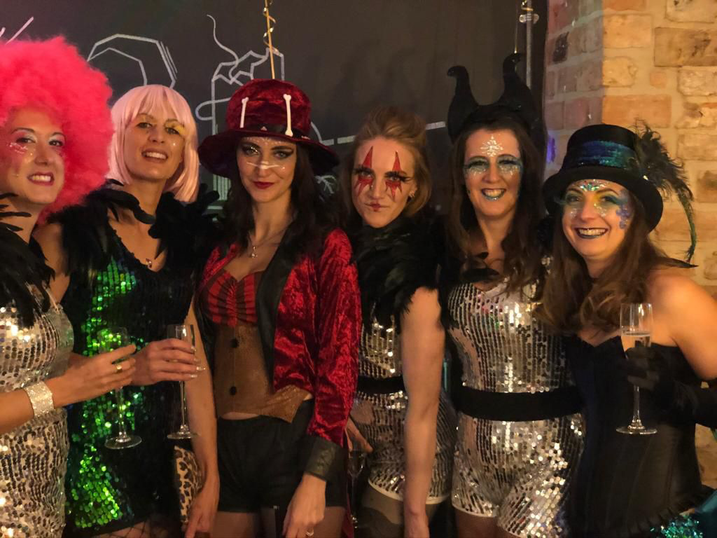 Six women dressed in colorful costumes and makeup at a party.