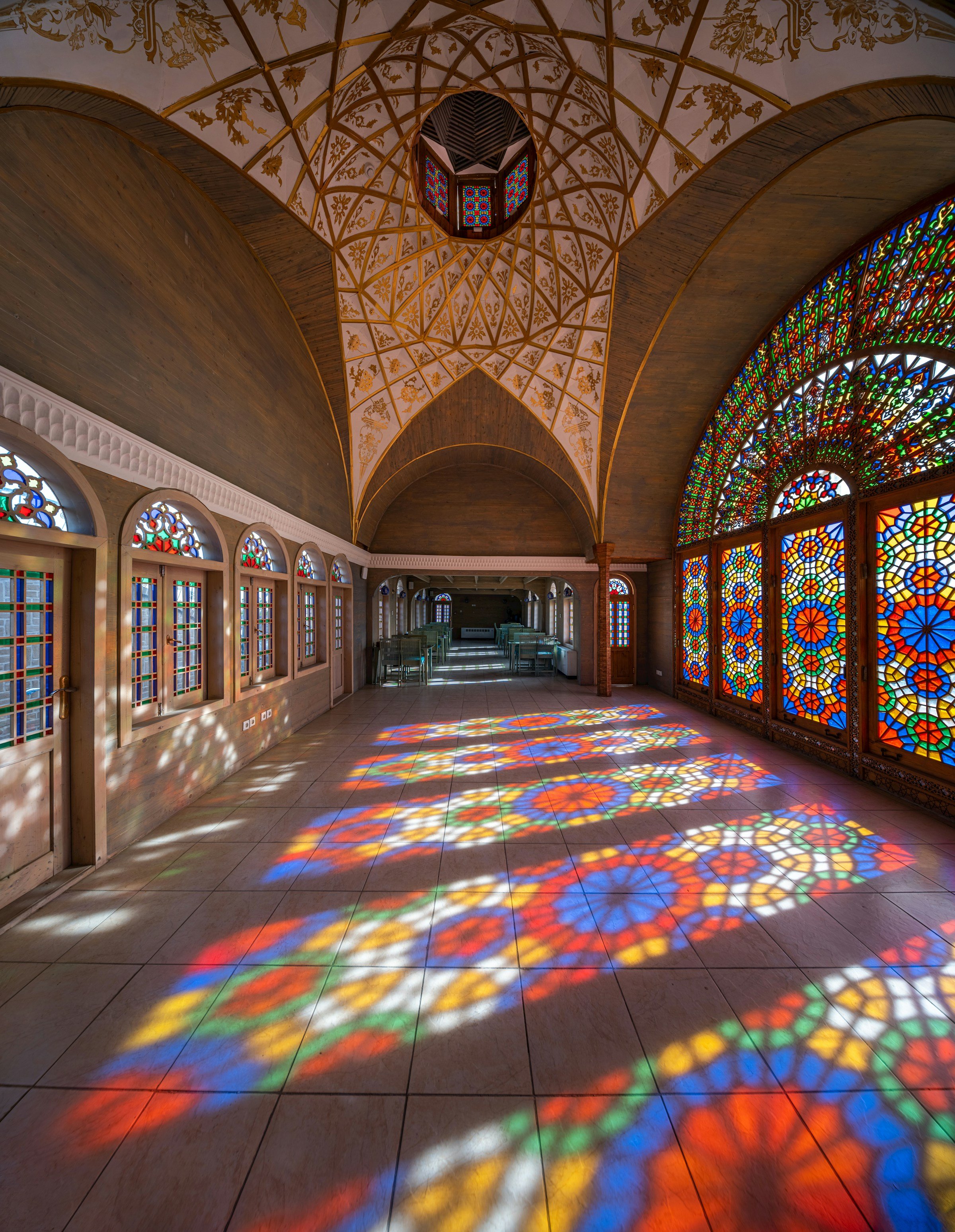 Sunlight passing through stained glass windows, casting colorful patterns on the tiled floor inside a spacious room with high, ornate ceilings.