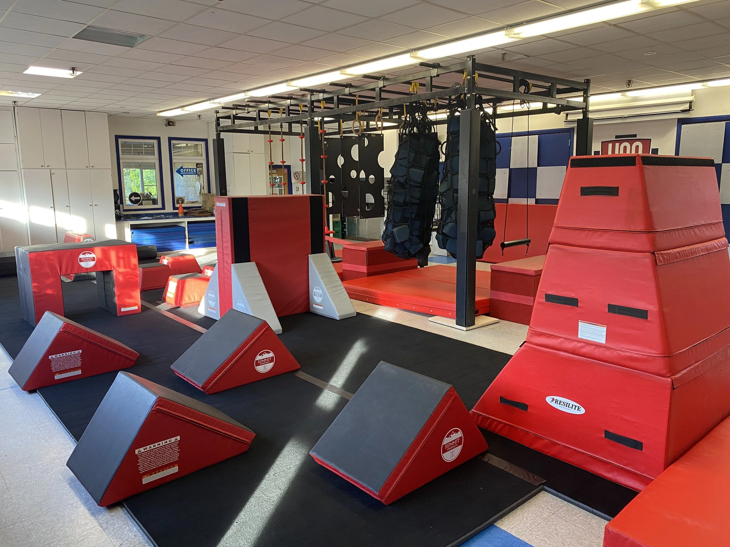 Indoor ninja obstacle course with climbing walls, padded mats, hanging rings, and foam blocks.