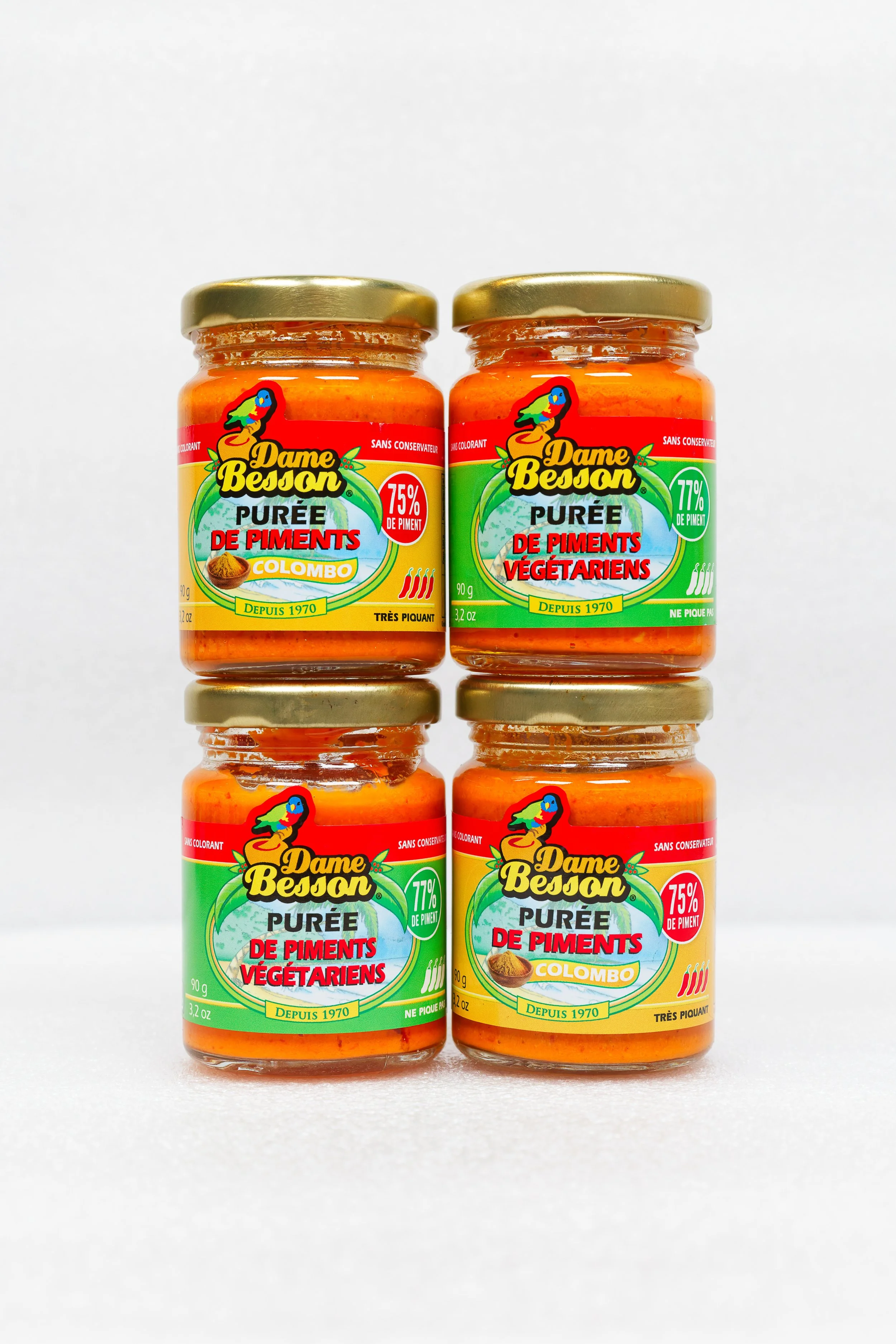 Quatre pots de purée de piments végétariens Dame Besson, avec étiquettes colorées jaune, rouge, vert, et blanc, affichant 75% et 77% de piment, alignés verticalement sur fond blanc.
