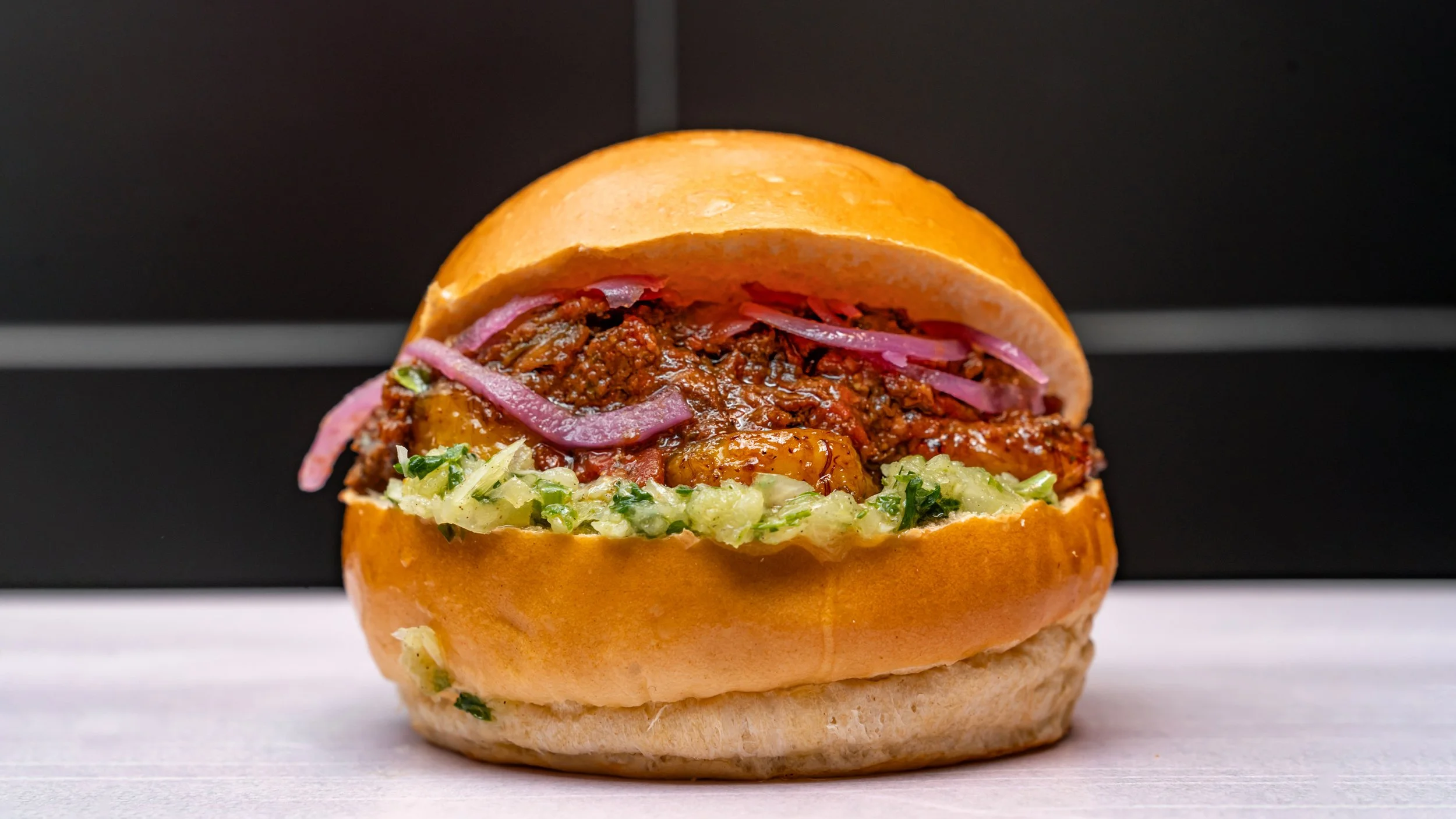 Un sandwich avec de la viande hachée, des oignons rouges, de la sauce, de la salade dans un bun.