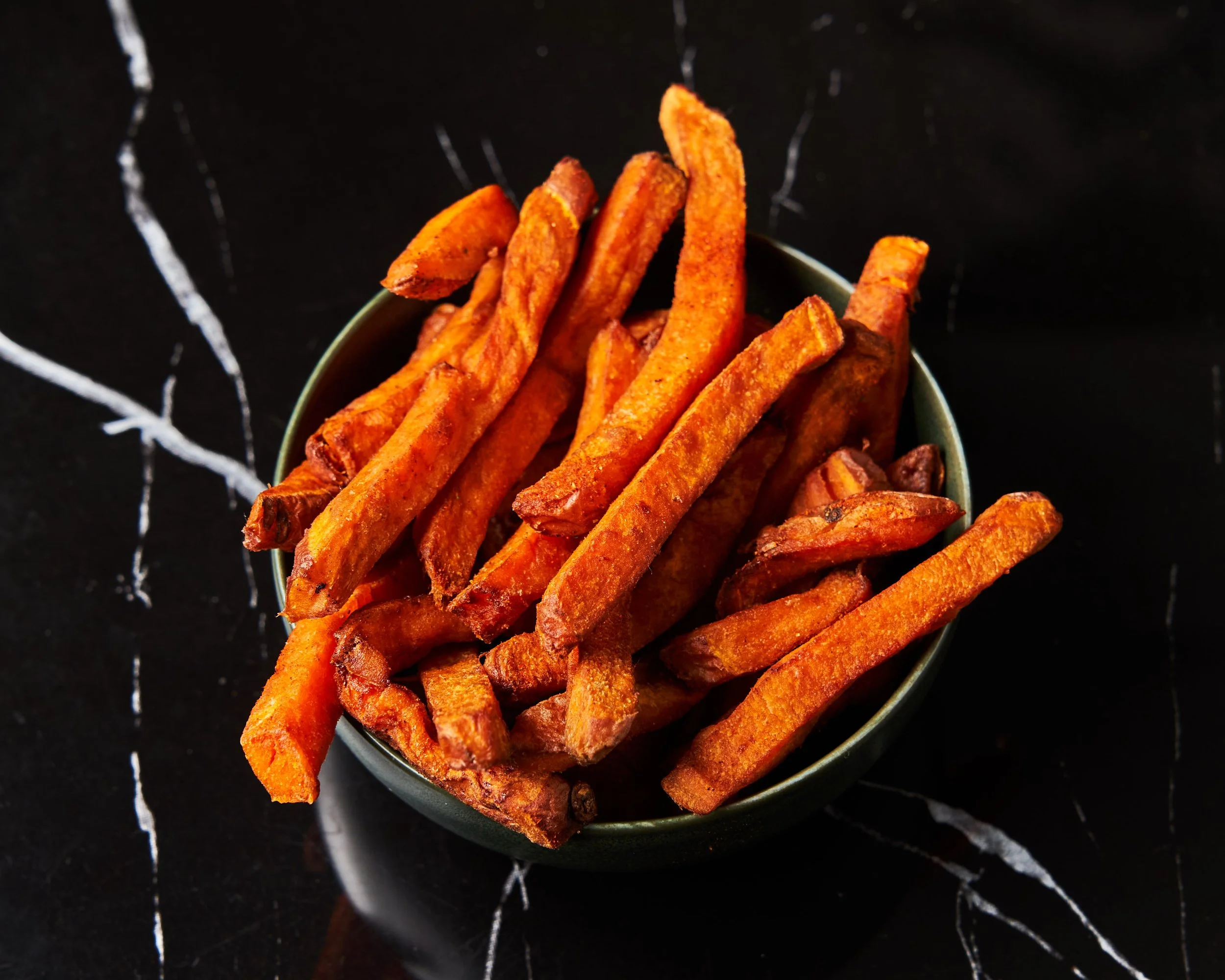 Frites de patate douce dans un bol gris foncé, sur un fond noir avec des lignes blanches
