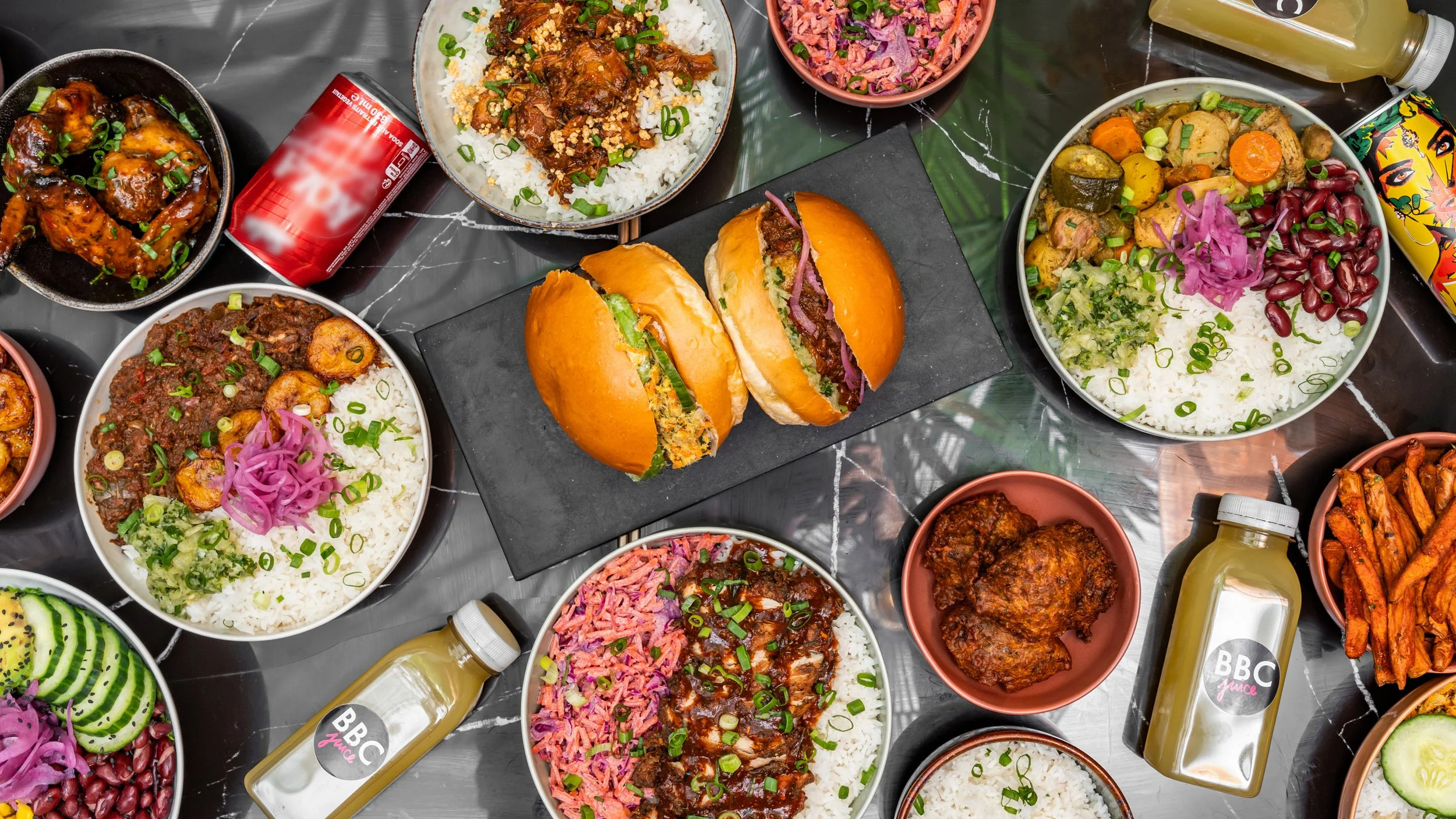 Variétés de plats de cuisine africaine comprenant du riz, des ragoûts, des légumes, des sandwichs et des boissons gazeuses sur une table en marbre.