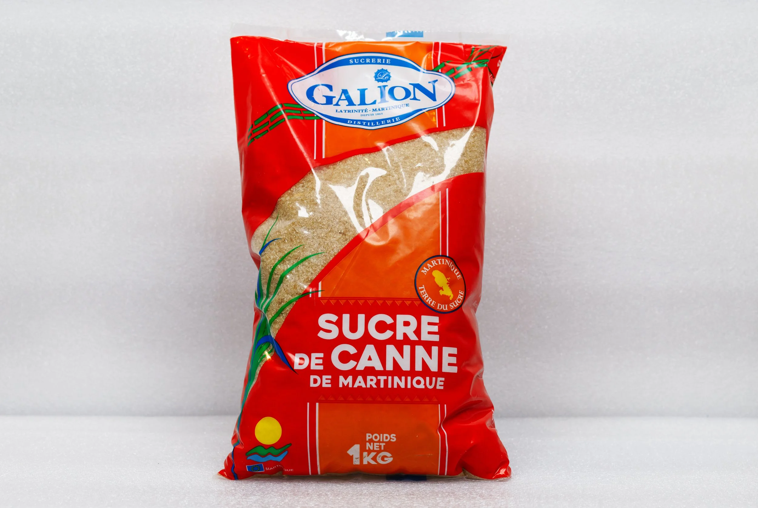 Sac de sucre en morceaux de 1 kg de couleur rouge avec un label bleu "Galion" et un motif vert, orange, et jaune, indiquant qu'il s'agit de sucre de canne de Martinique.