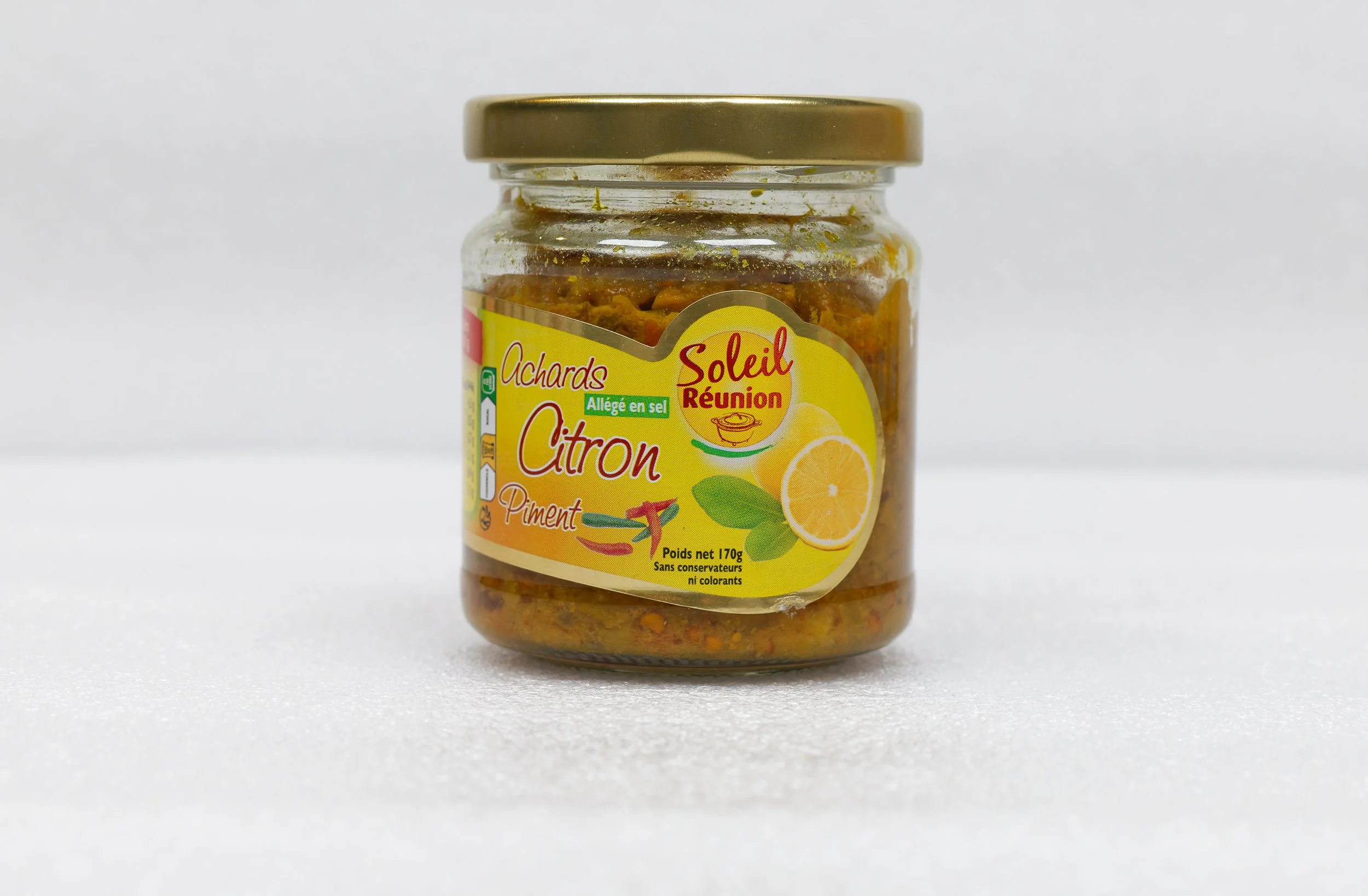 Bocal transparent de confiture ou condiment avec une étiquette jaune indiquant 'Achards Citron Piment', contenant une préparation colorée avec des morceaux visibles, posé sur fond blanc.