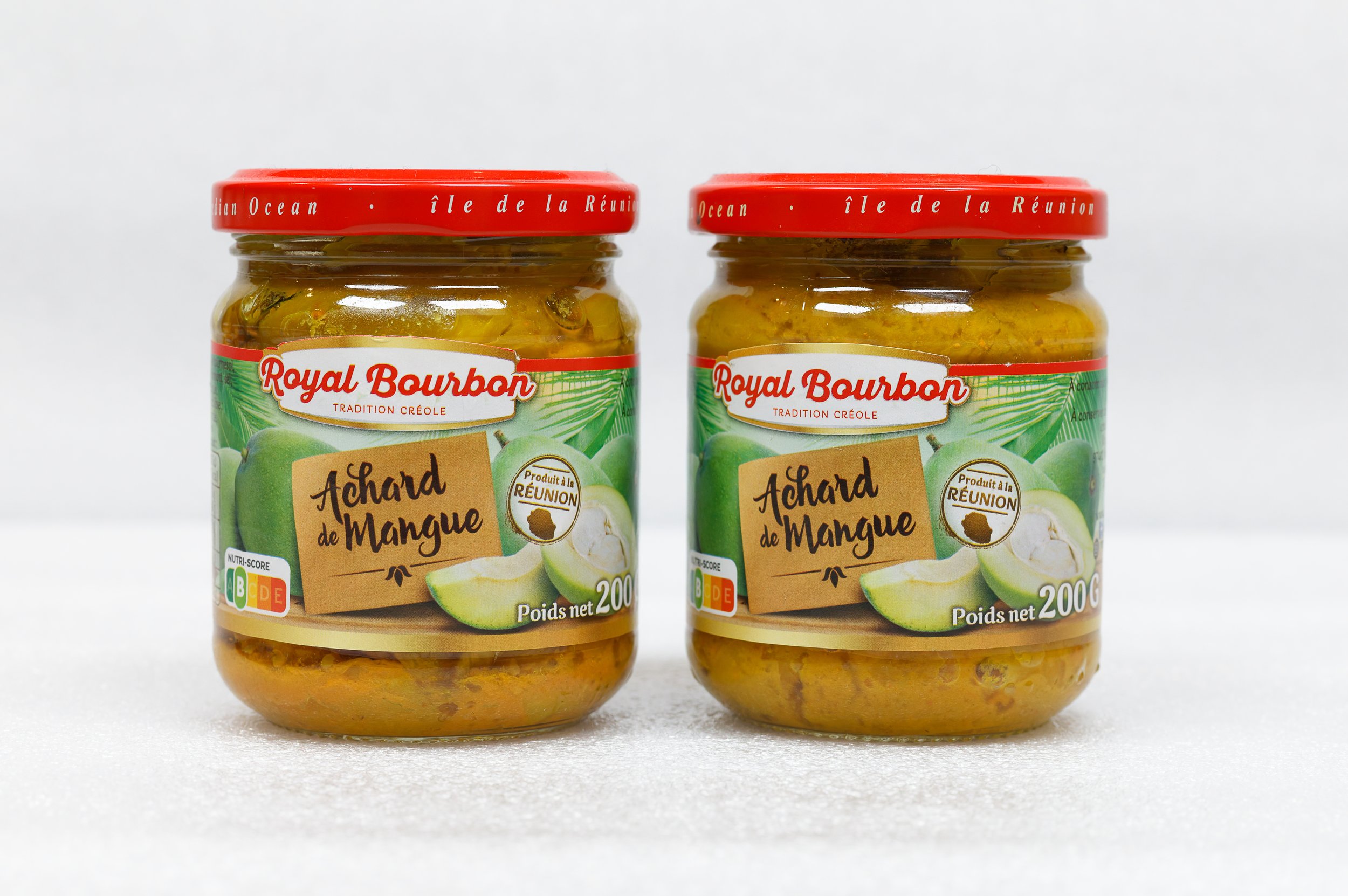 Deux pots de confiture d'achards de mangue avec des étiquettes colorées, marqués 'Royal Bourbon' et 'Produit à la Réunion', posés sur une surface blanche.