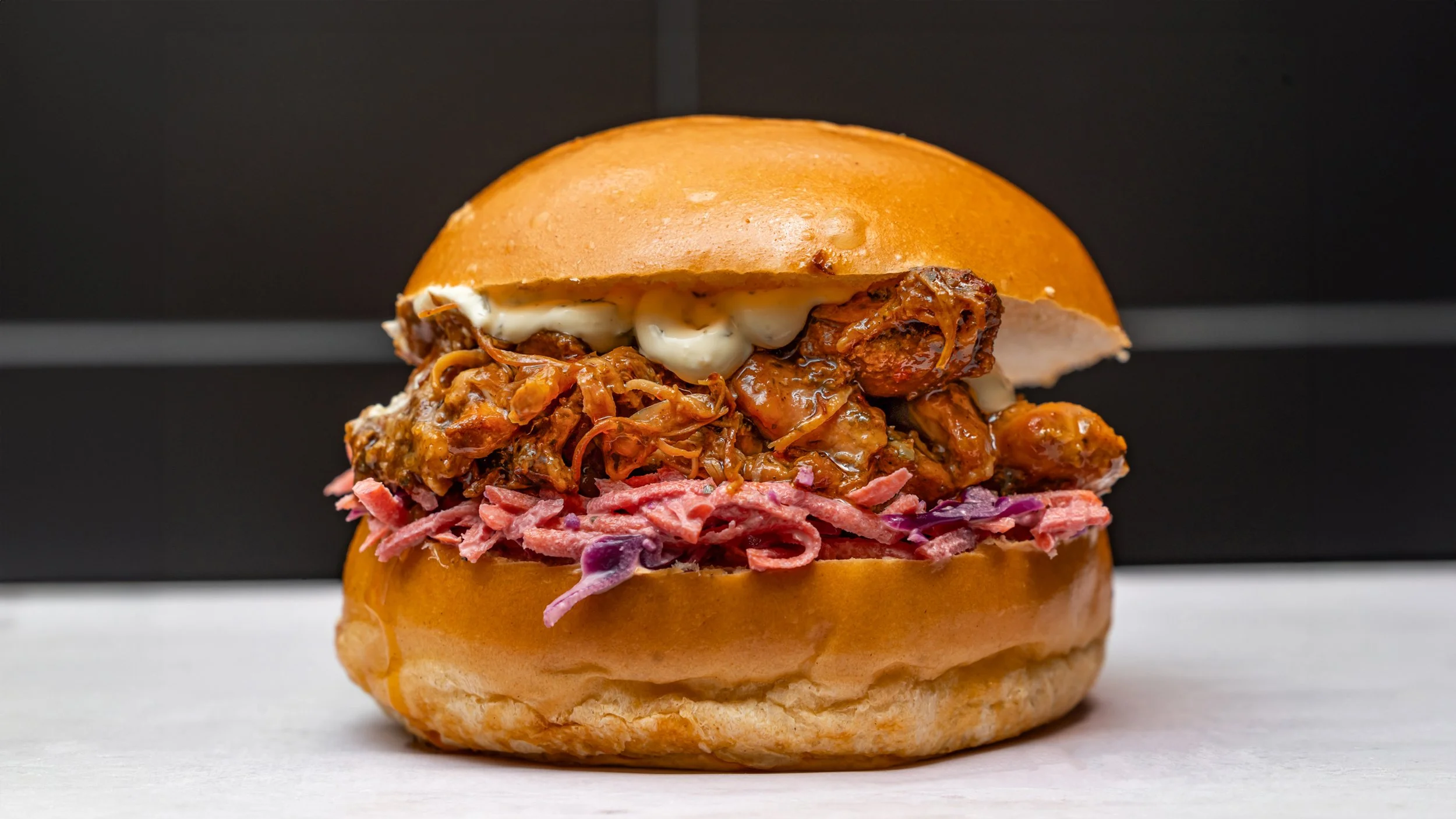 Un sandwich garni de viande effilochée, de sauce, de coleslaw et de viande hachée, dans un bun doré.