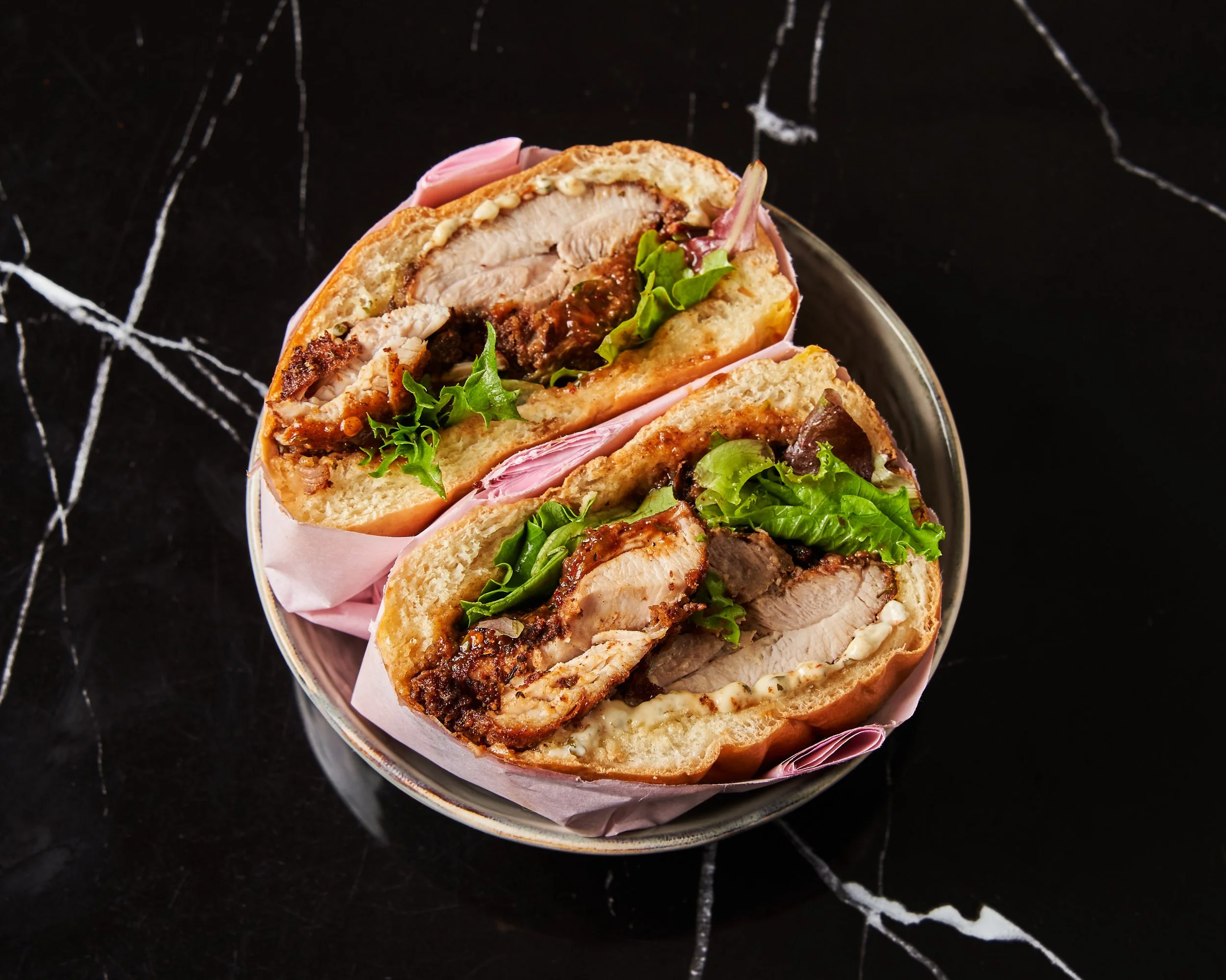 Un sandwich avec de la viande, de la salade, et une sauce, présenté dans un bol.