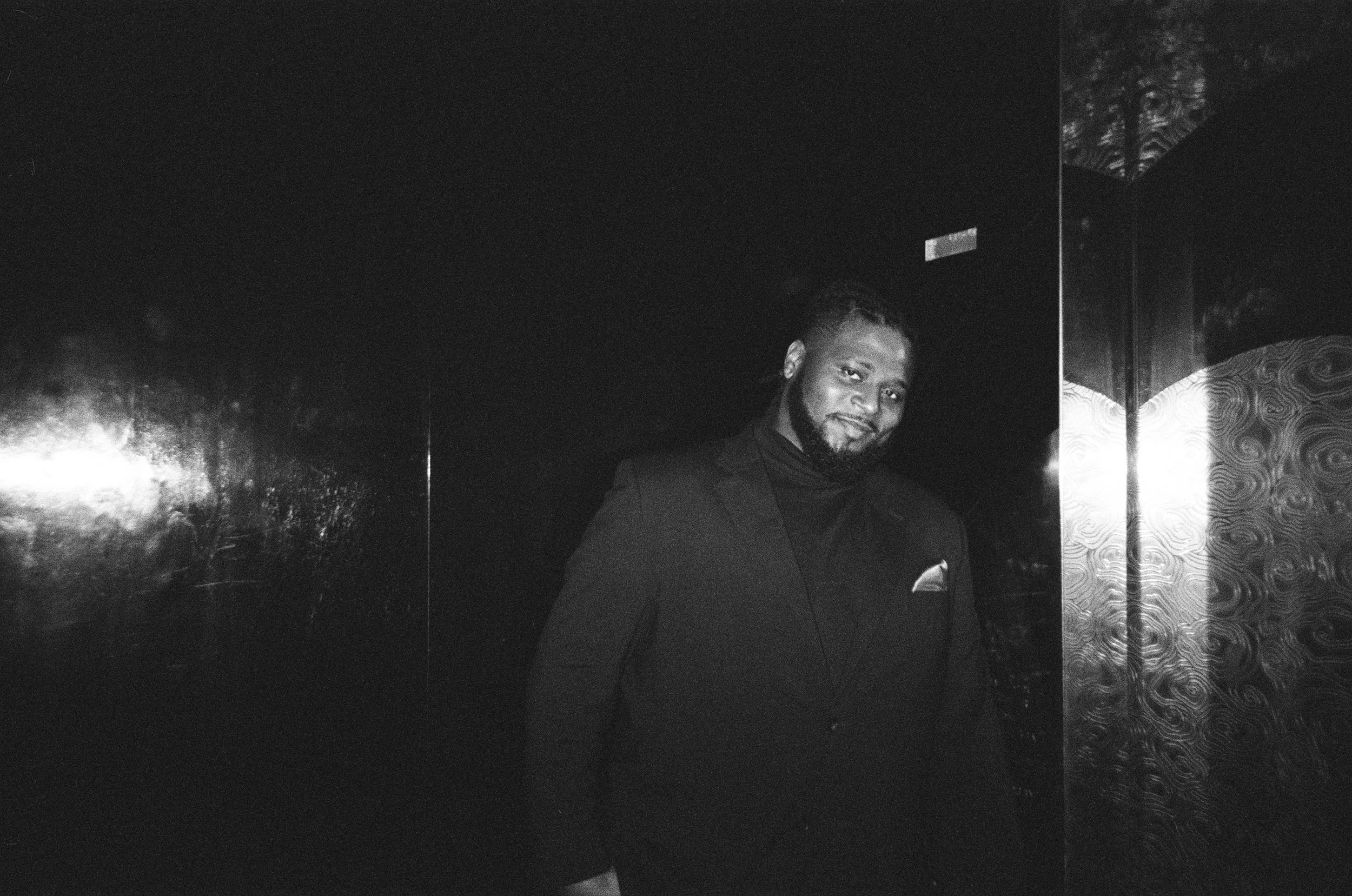 Jonathan Gilbert in formal black suit smiling in front of dark reflective wall