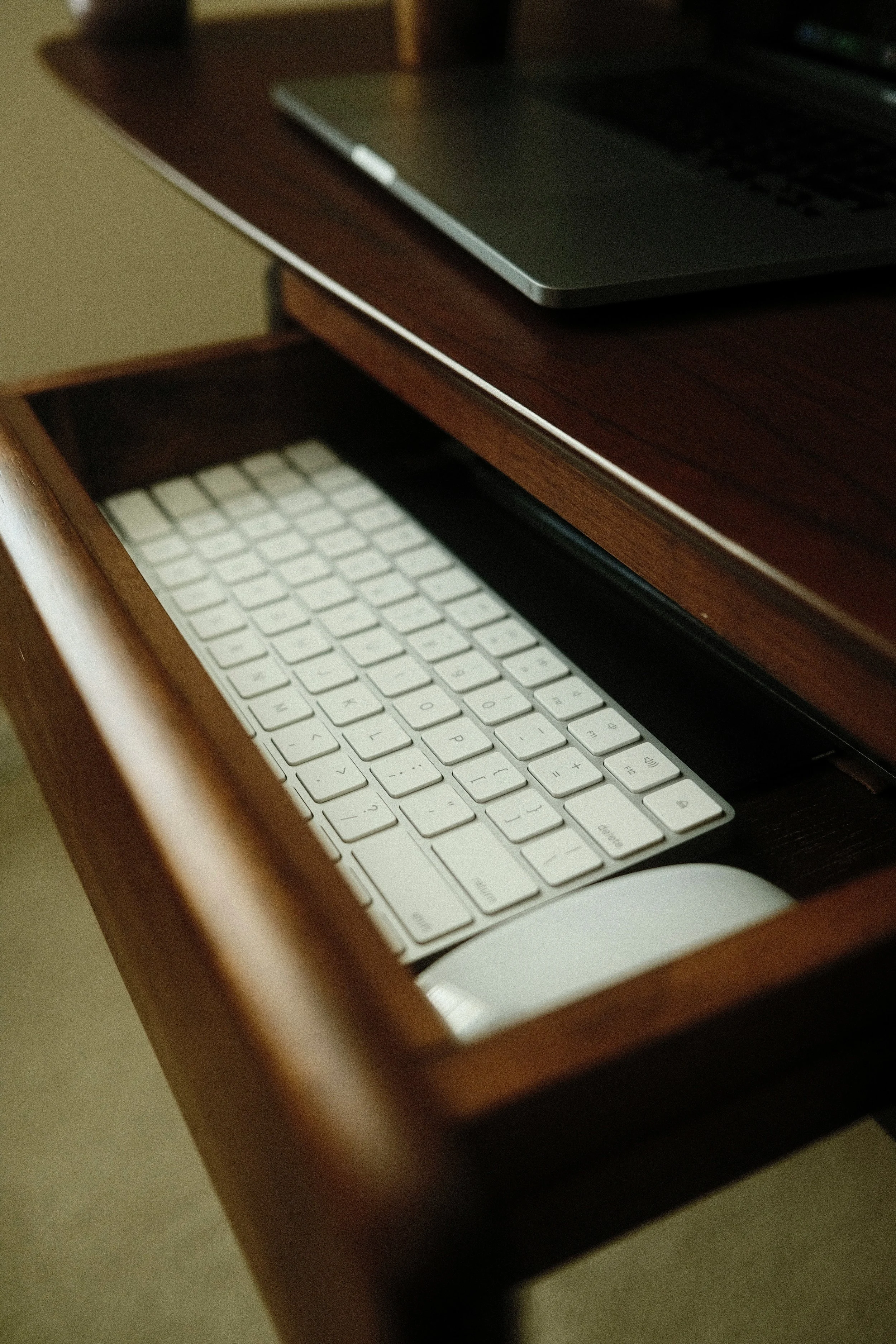Clavier et souris blanche rangés dans un tiroir en bois sous un bureau en bois.