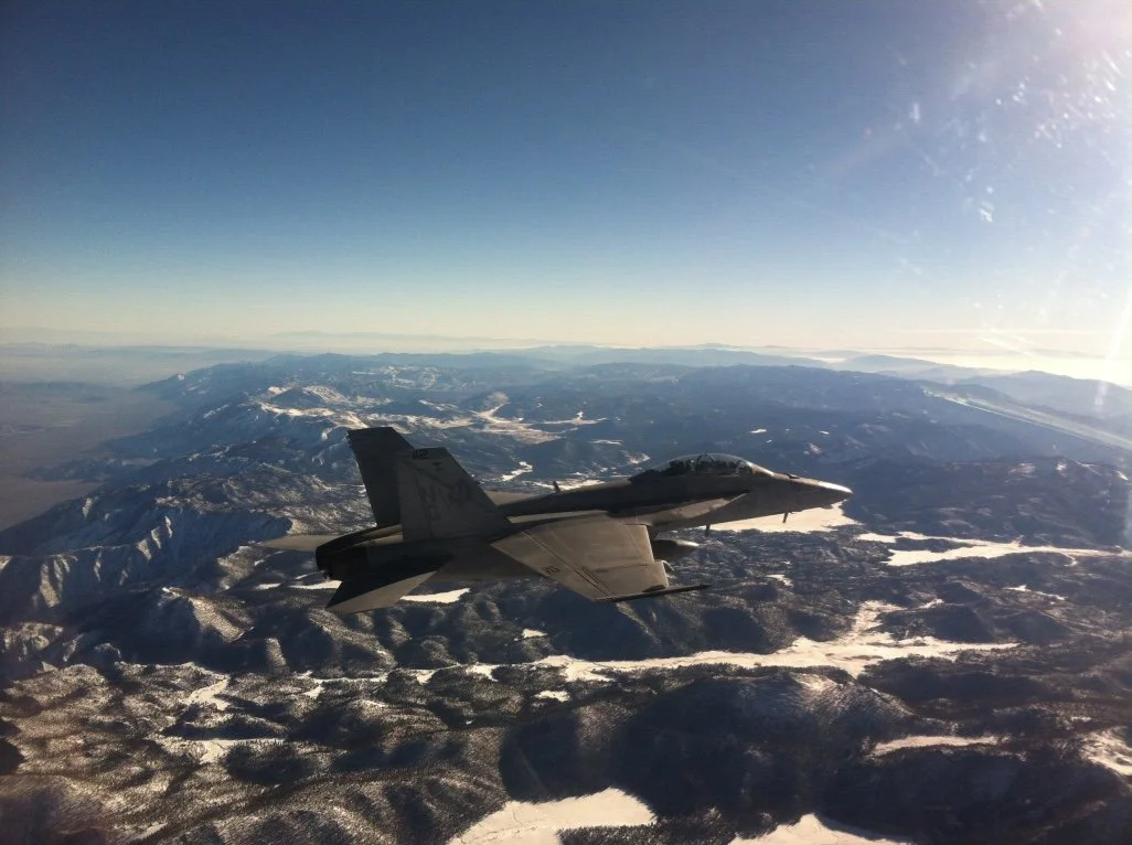 A fighter jet flying over snow-covered mountains and valleys during daytime.
