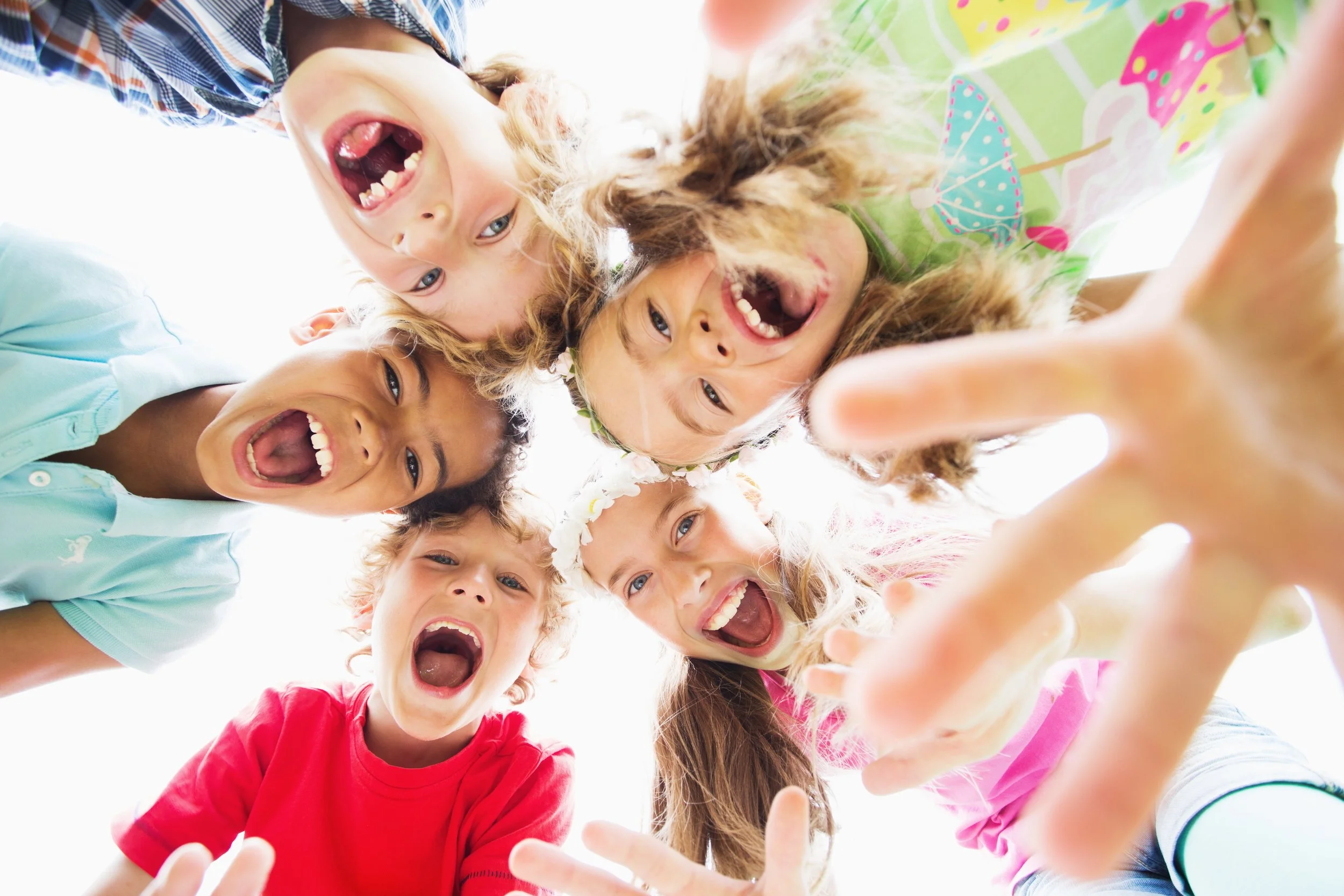 Group of children looking down at the camera, smiling and laughing, with some reaching out toward the camera.