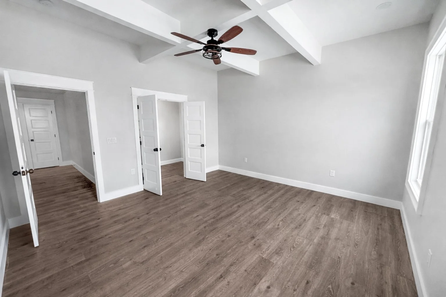 Empty room with white walls, wood flooring, a ceiling fan, and multiple doors leading to other rooms.