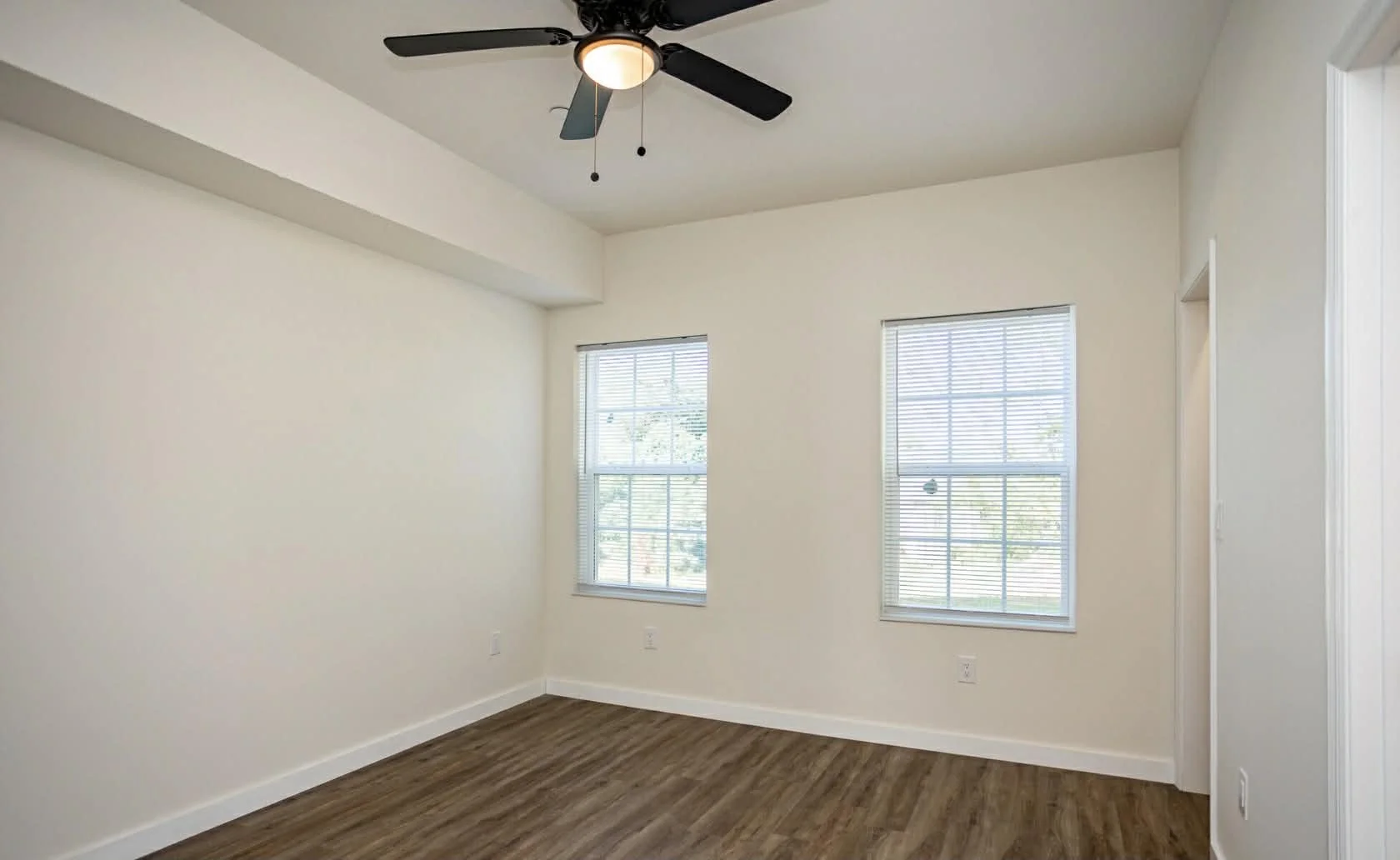 Empty room with two windows, a ceiling fan, hardwood floor, and white walls.