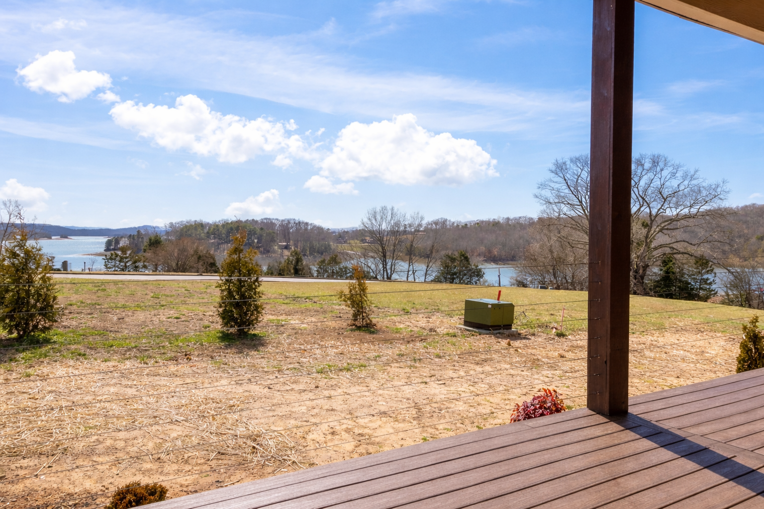 View from a porch overlooking a flooded area with trees and water, under a blue sky with clouds.